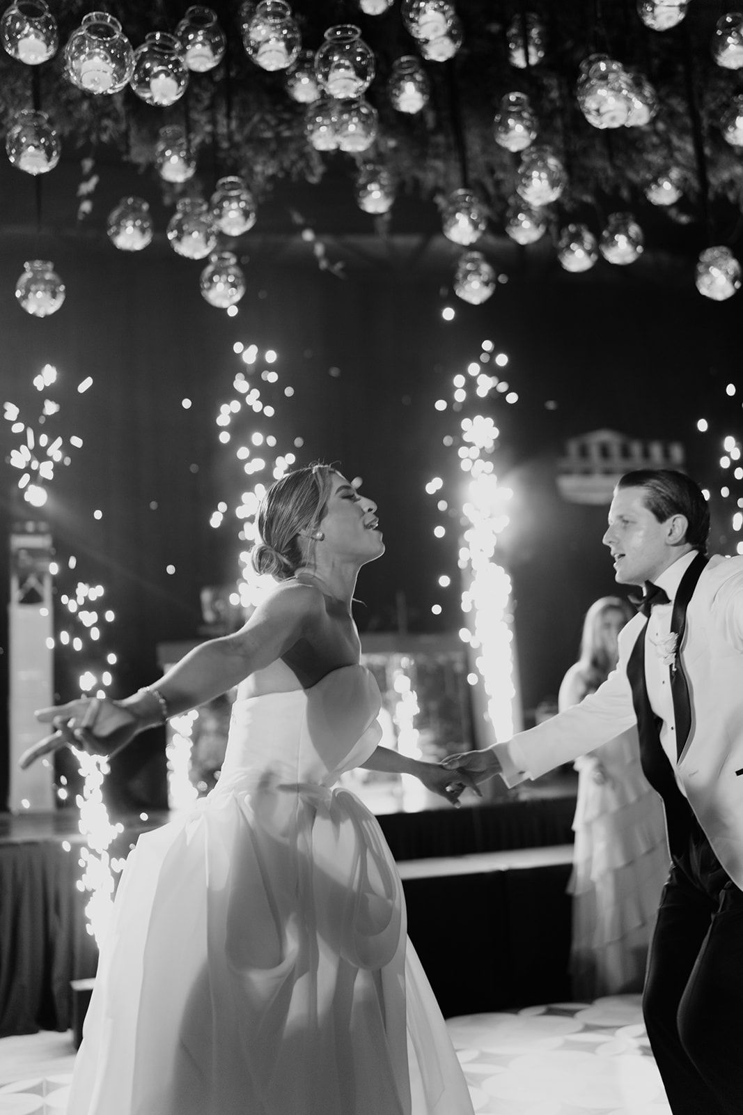 Black and white photo of bride and groom sharing first dance surrounded by sparkling fireworks and hanging lights.