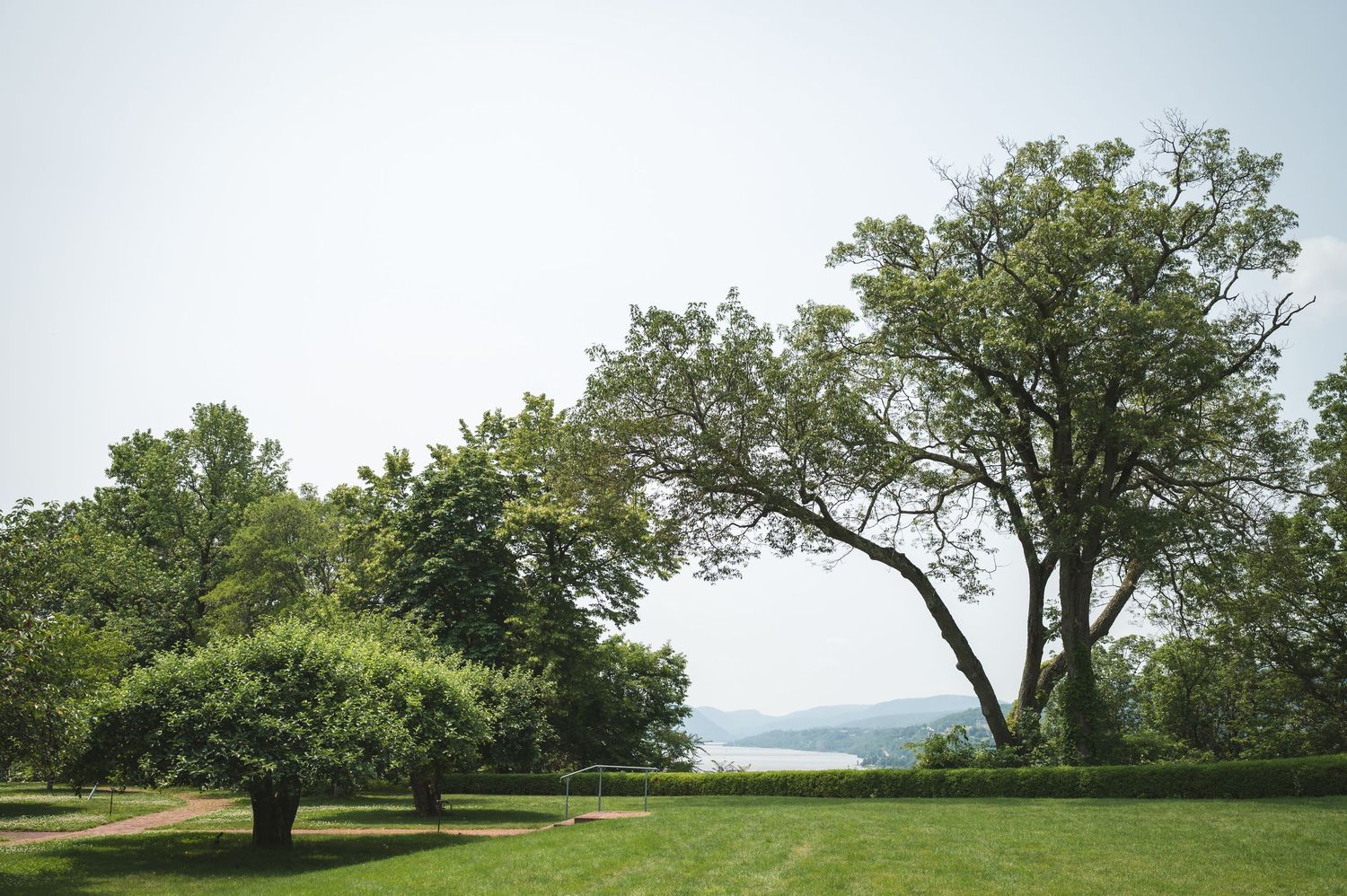 A panoramic view of the Hudson River framed by mature trees on a grassy ceremony space hilltop at Boscobel in Garrison, NY in Hudson Valley.