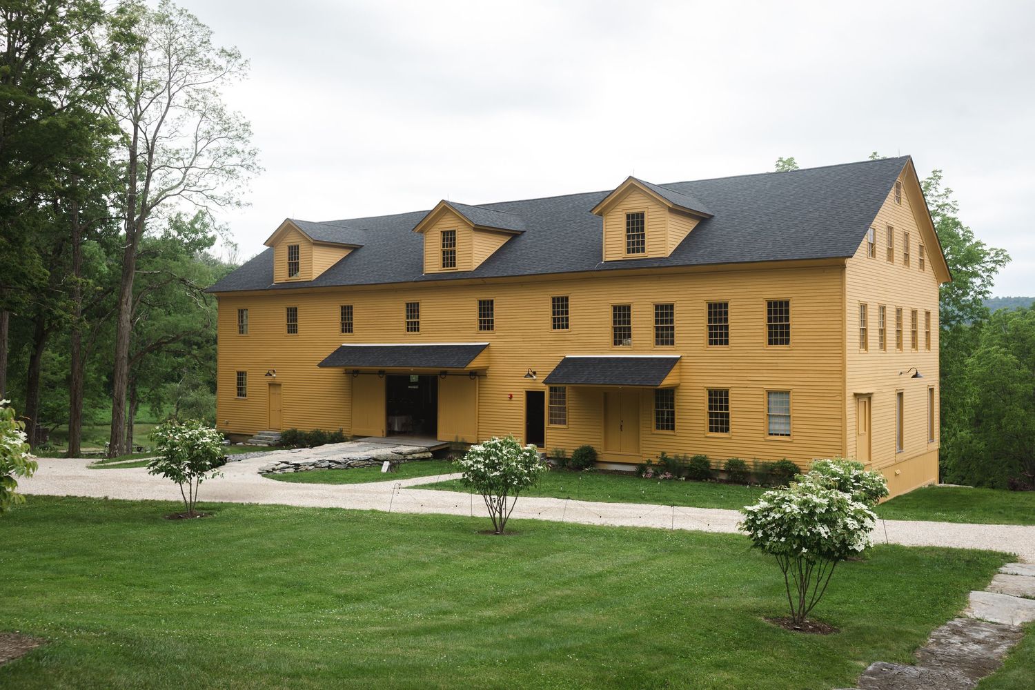 Large yellow historic building at The Ruins at Sassafras with dormers and black shutters on a landscaped lawn in the Hudson Valley.