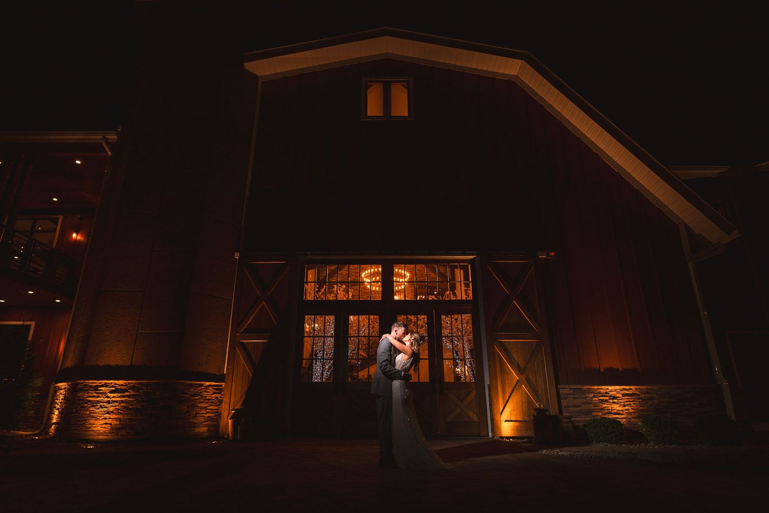 Flash portrait of couple as warm light glows through large windows of The Barn at Villa Venezia at night in Middletown, NY in Hudson Valley.