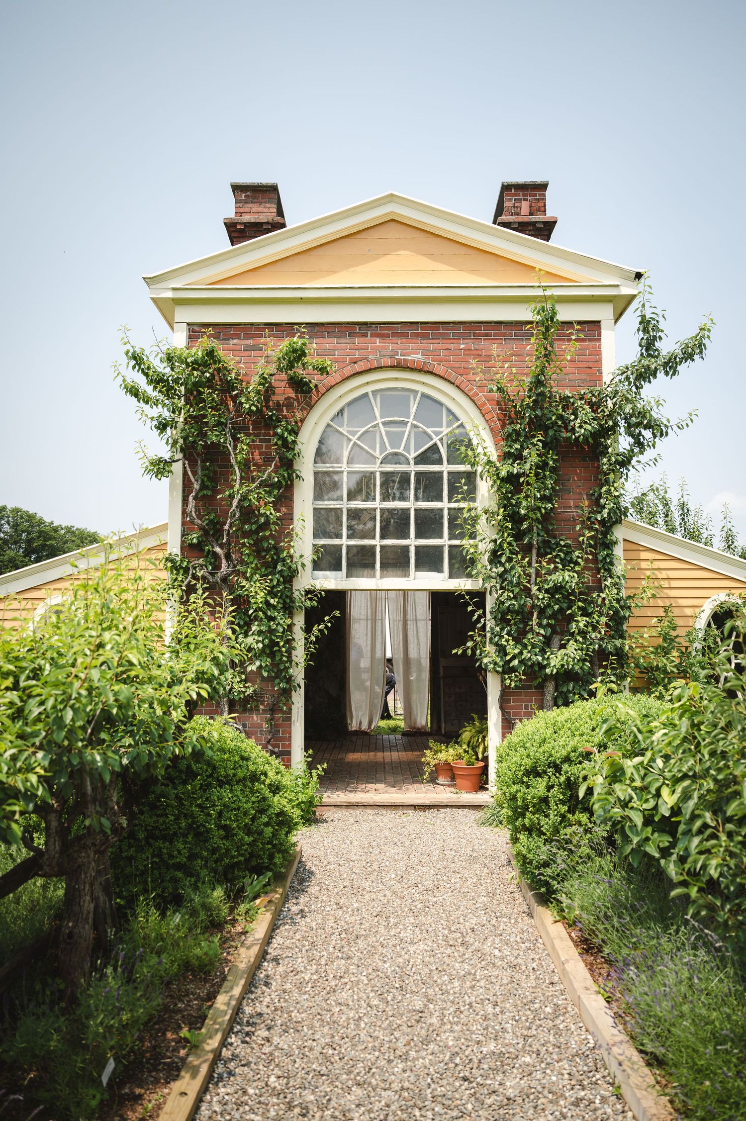 Four views of a classic brick country house with arched windows and gravel pathway leading to entrance surrounded by lush gardens.