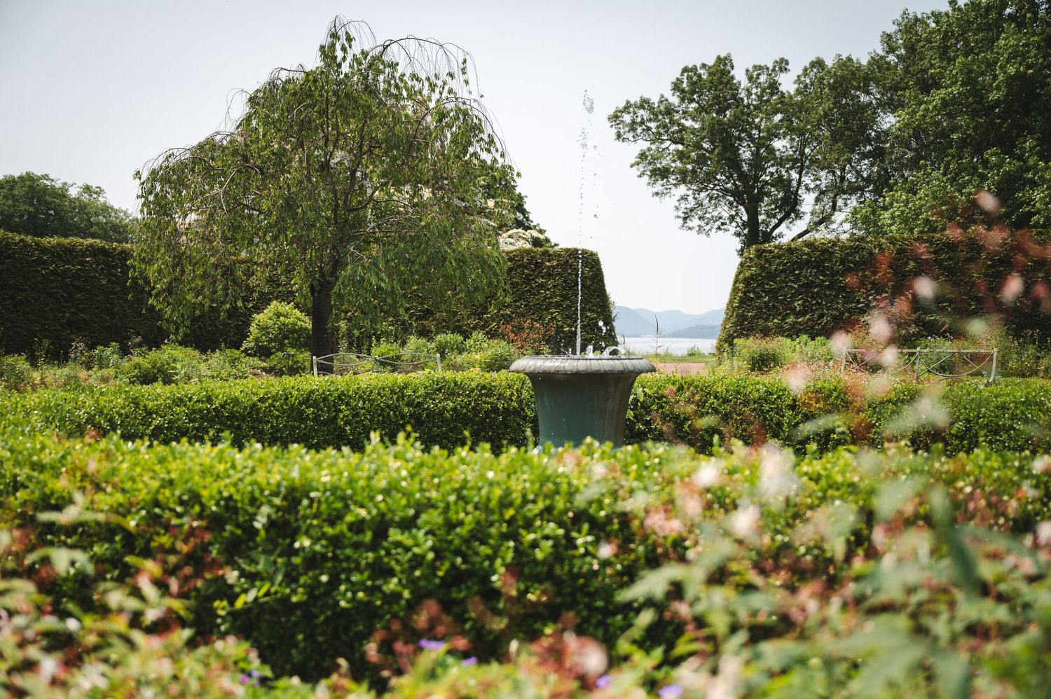 Lush garden filled with blooming flowers and manicured hedges leading to view of Hudson River at Boscobel in Garrison, NY in Hudson Valley