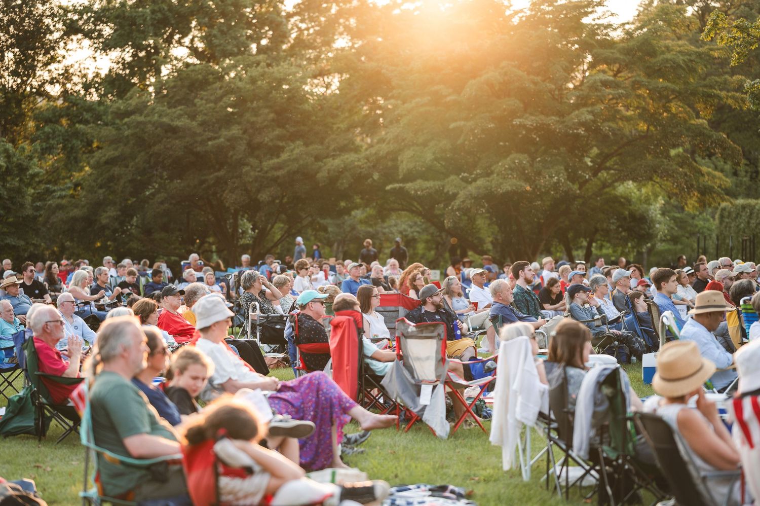 Large crowd of guests seated at outdoor tables during sunset at an elegant garden party event at Boscobel in Garrison, NY in Hudson Valley.