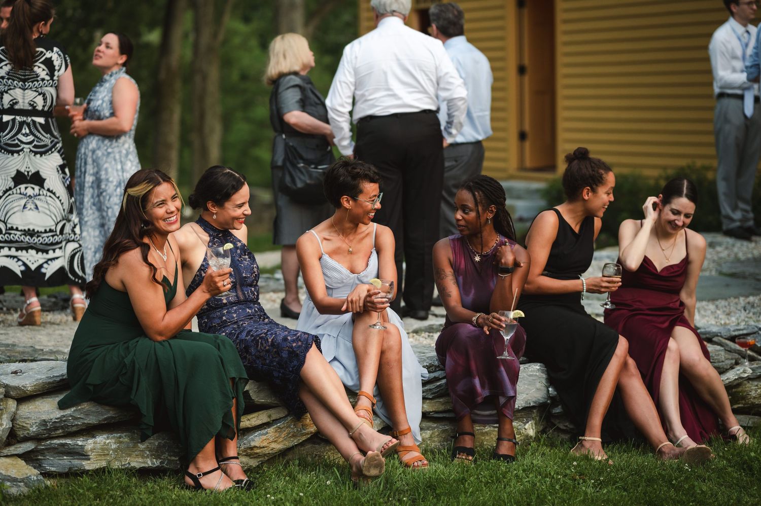 Group of friends sitting together on outdoor steps while enjoying a relaxed summer wedding reception at the Ruins at Sassafras in New York.