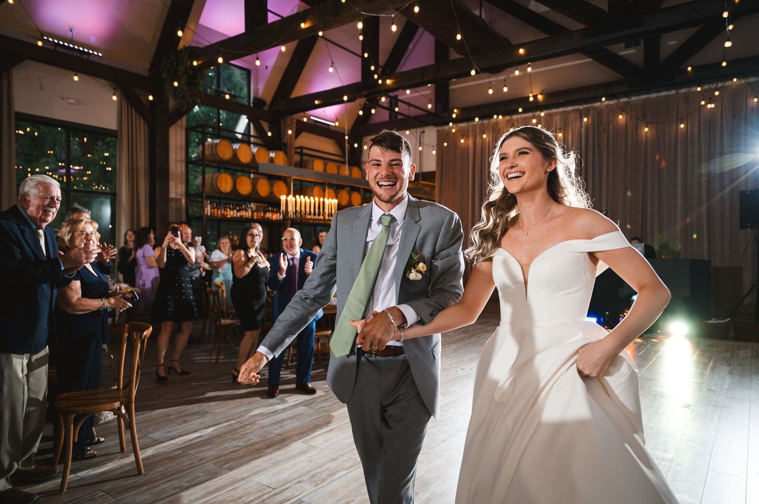 Wedding couple laughing during entrance to first dance while guests cheer in the background at The Barn at Villa Venezia in Middletown, NY.