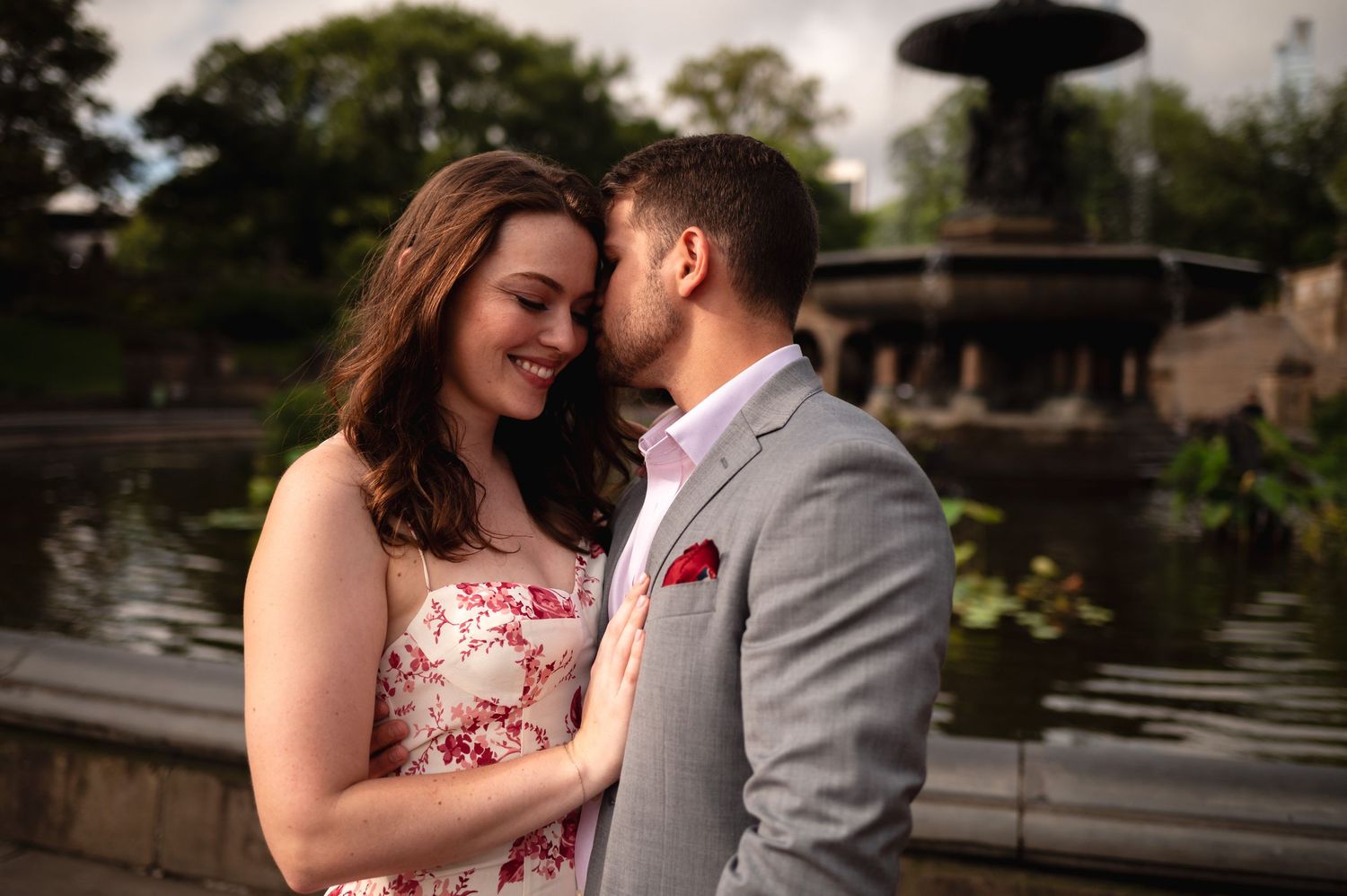 A romantic couple embraces in front of Bethesda fountain in Central Park during morning golden hour engagement photos in New York City.