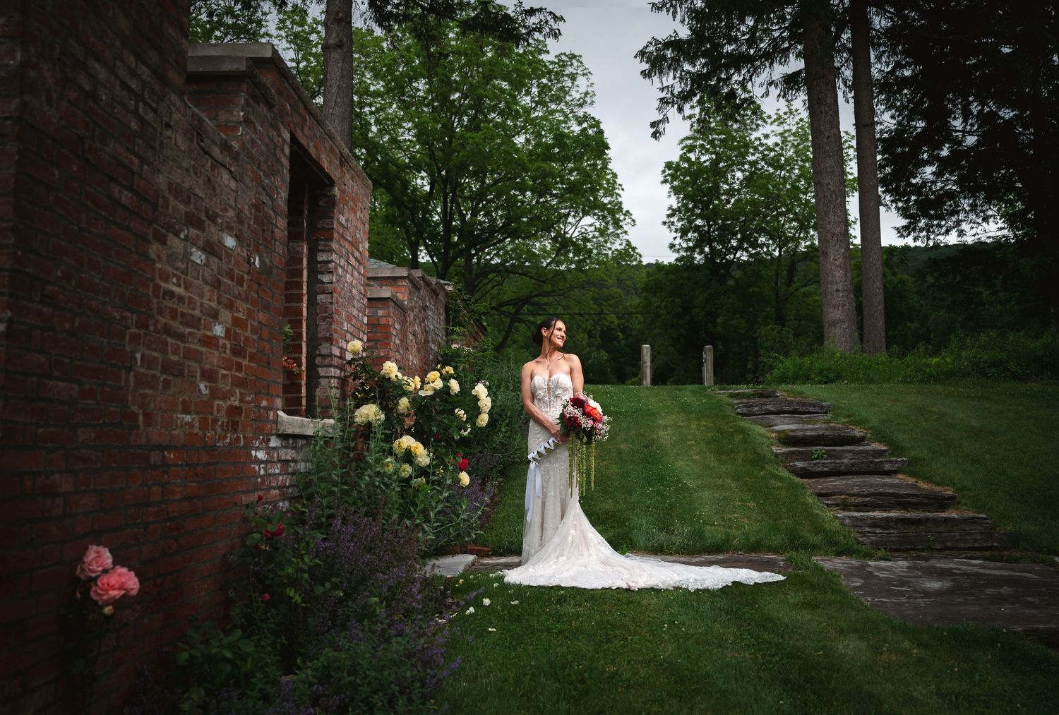 Flash portrait of bride in a white wedding gown on rustic garden steps surrounded by lush greenery and stone walls at The Ruins at Sassafras
