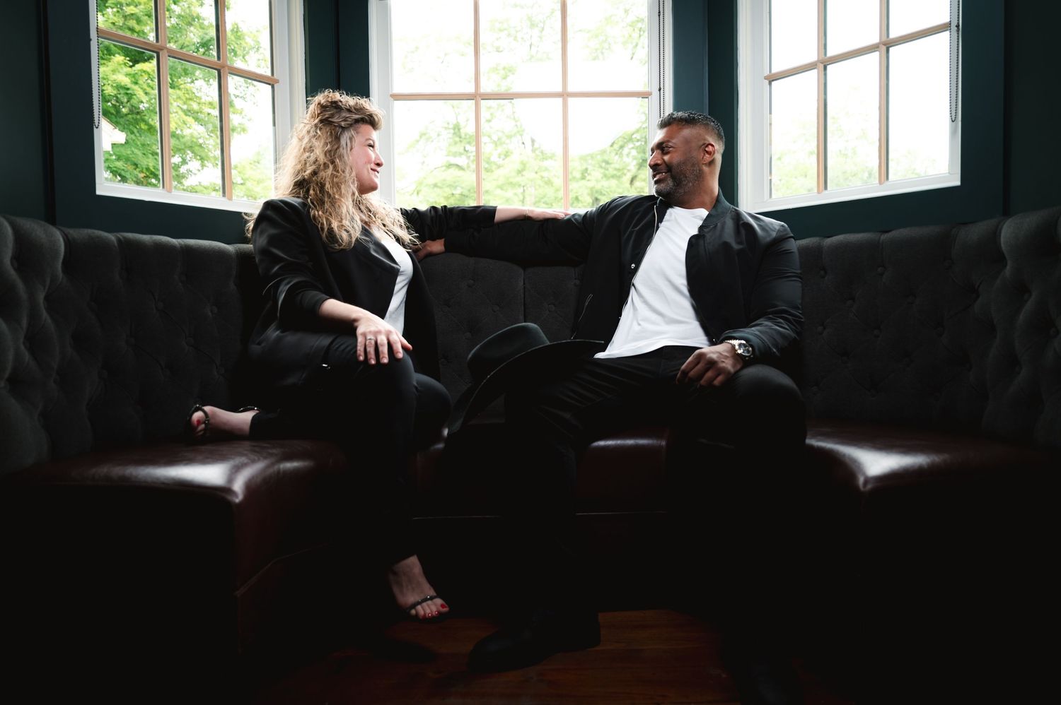 Two people embrace on a leather sofa in natural window lighting.