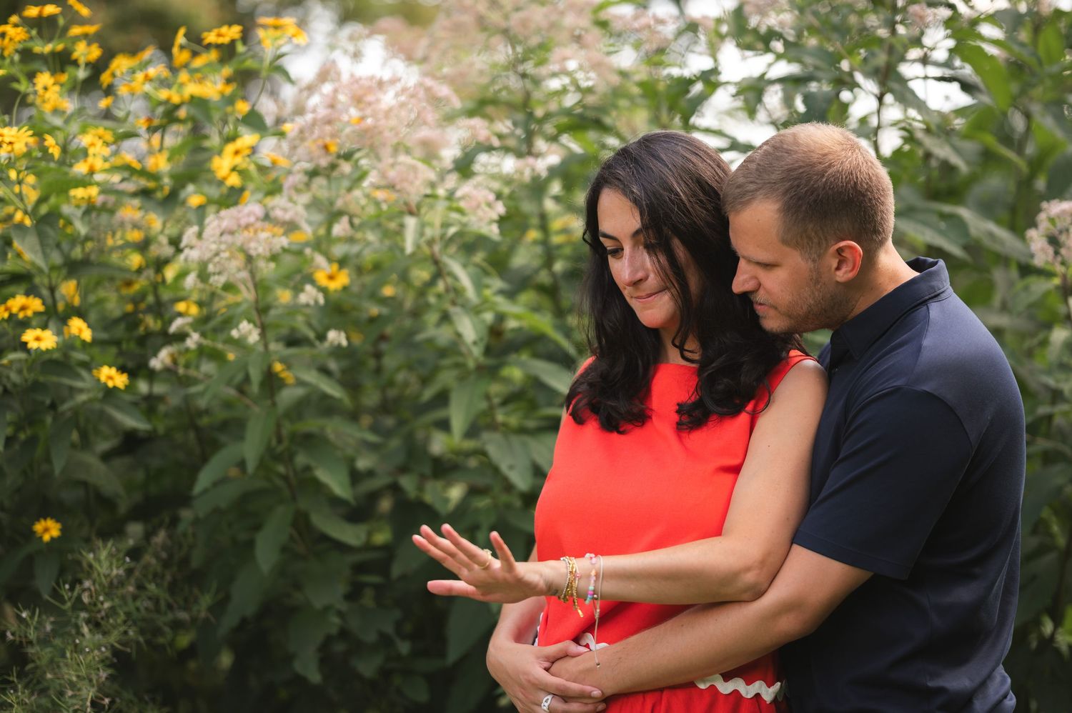 Couple embraces lovingly in a garden with vibrant yellow flowers and greenery in the background.