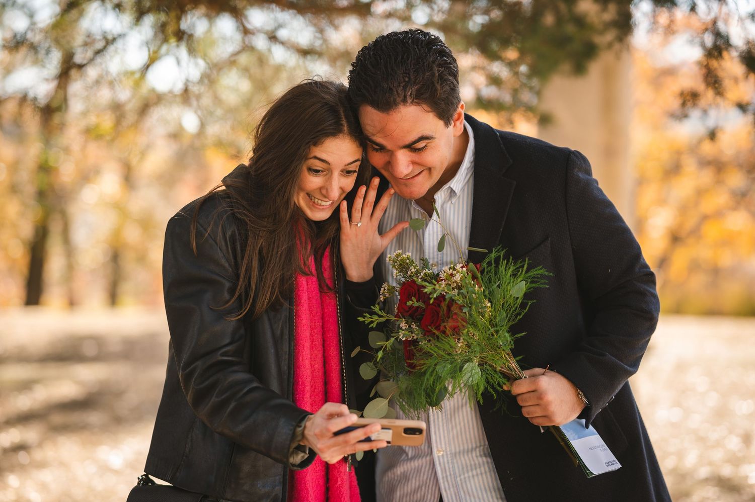 Couple showing engagement ring to family during autumn while holding a bouquet of red roses at Storm King Art Center in the Hudson Valley.