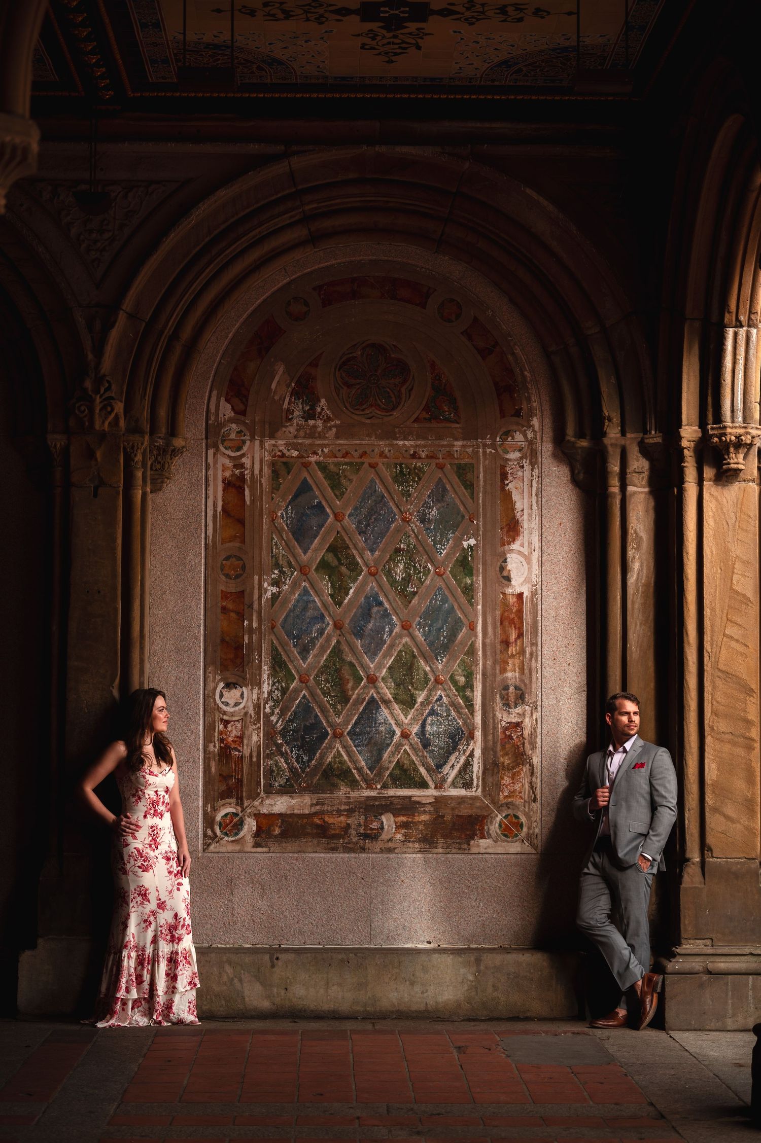 A couple poses against dramatic stone archways and stained glass windows in a romantic engagement photo sequence.