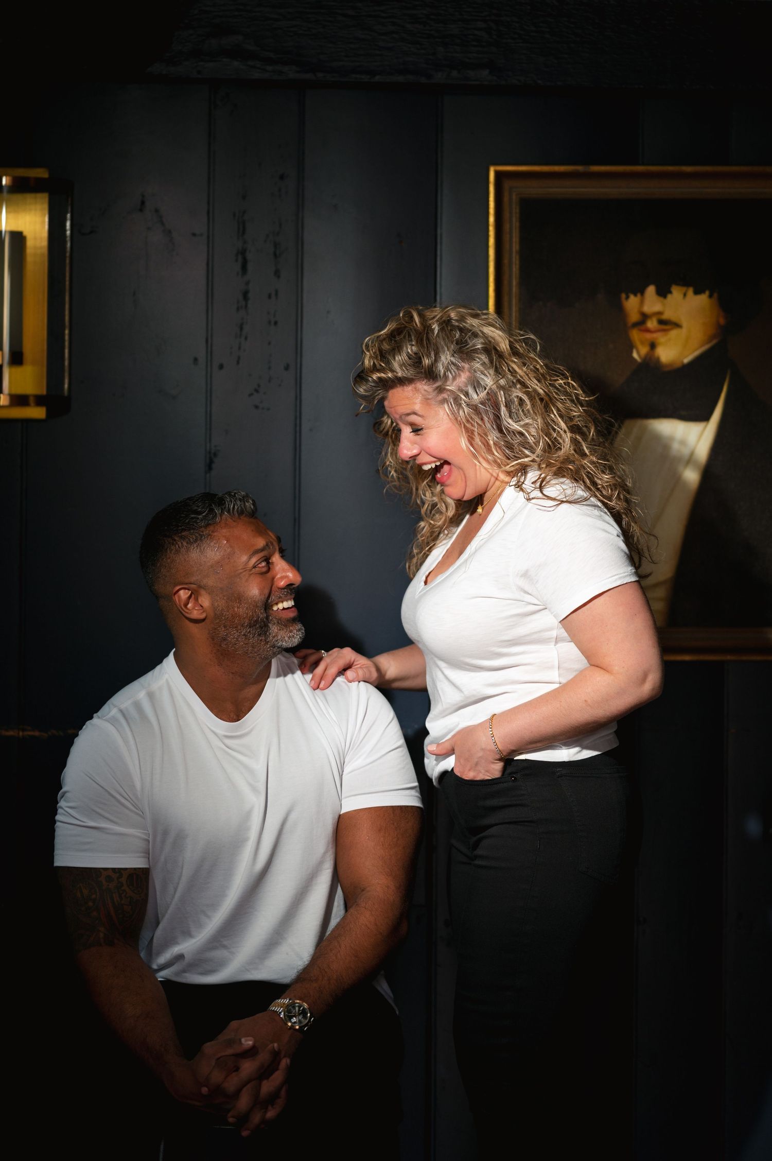 A couple laughs together during a candid photo in front of dark blue wall in the Bird&Bottle Inn in Garrison, NY in the Hudson Valley.