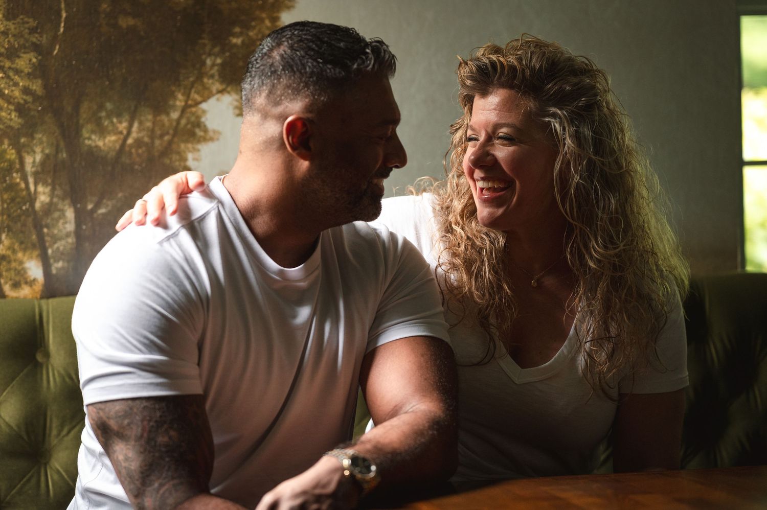 A couple in moody lighting share an intimate moment on a sofa near a window.