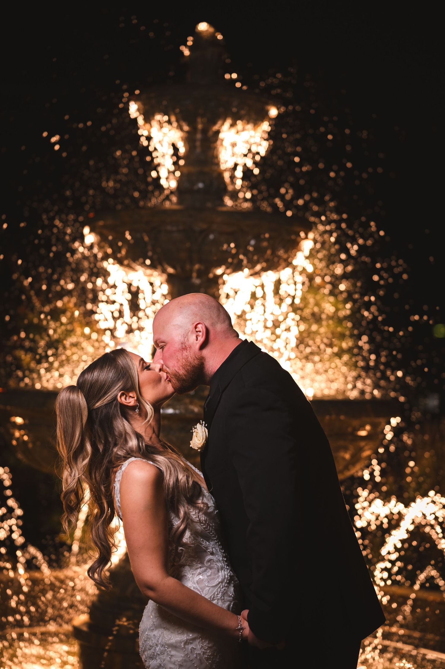 Romantic wedding couple kissing at night in front of illuminated fountain creating magical light effects in northern NJ wedding.