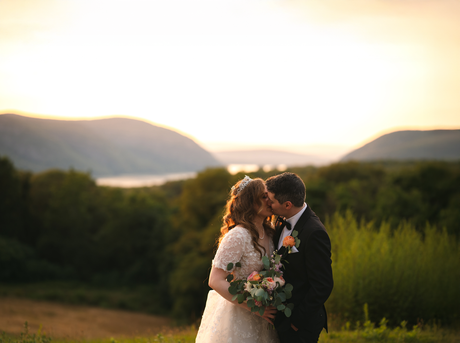 Wedding couple shares an intimate moment at sunset in front of scenic mountains and the Hudson River at The Garrison in Garrison, NY.