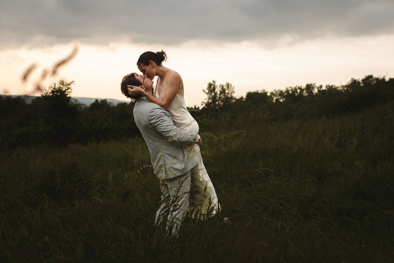 A couple spins and kisses in a grassy meadow at sunset with rolling hills in the background at Ruins at Sassafras, New Lebanon, NY.