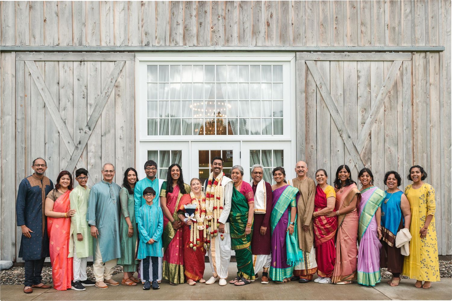Family photo wearing traditional Indian wedding attire in front of barn and large entrance doors at Fortune Valley Manor in Saugerties, NY.
