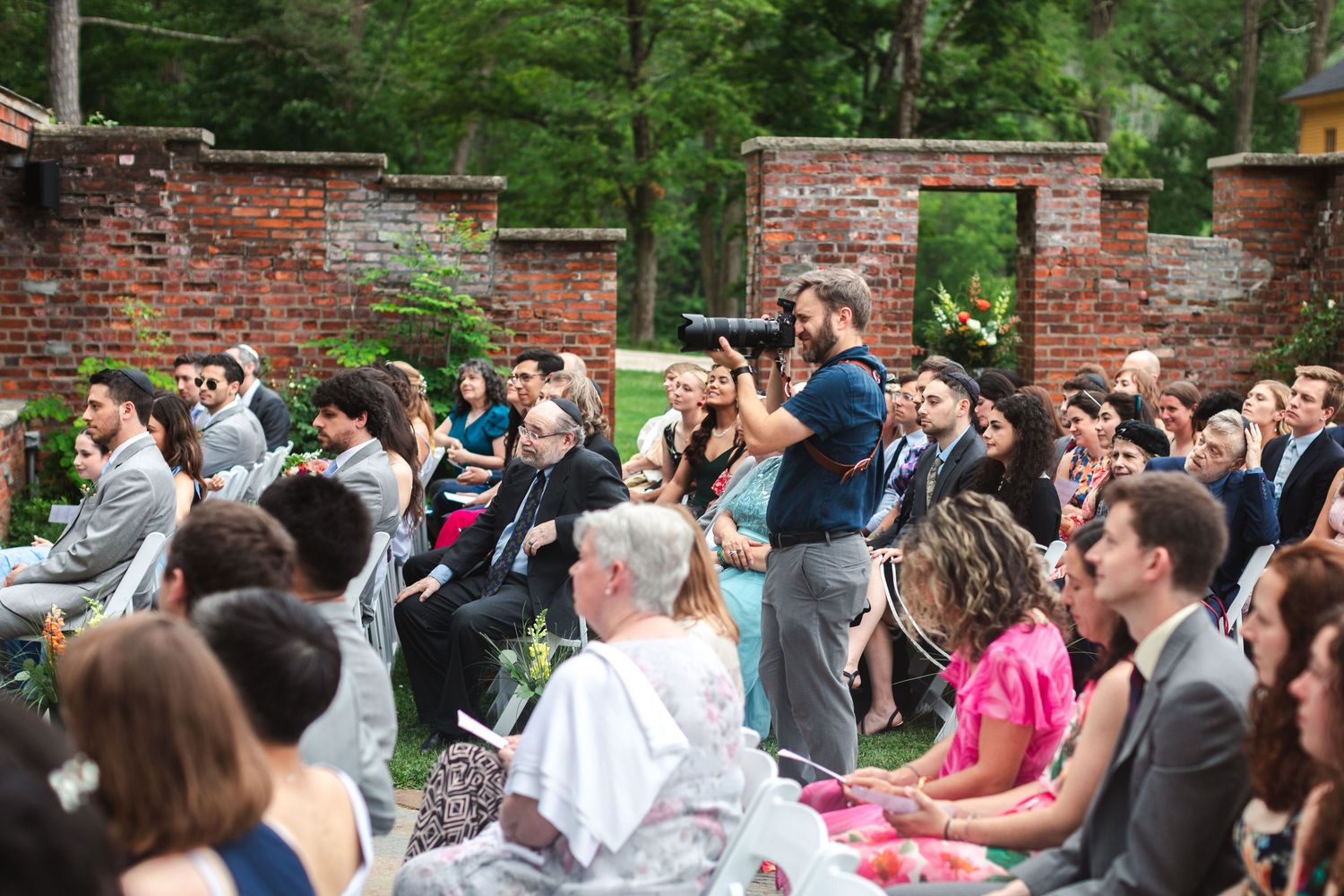 Matthew Rigby photographing a ceremony next to brick walls in garden with guests at The Ruins at Sassafras New Lebanon, NY in Hudson Valley.