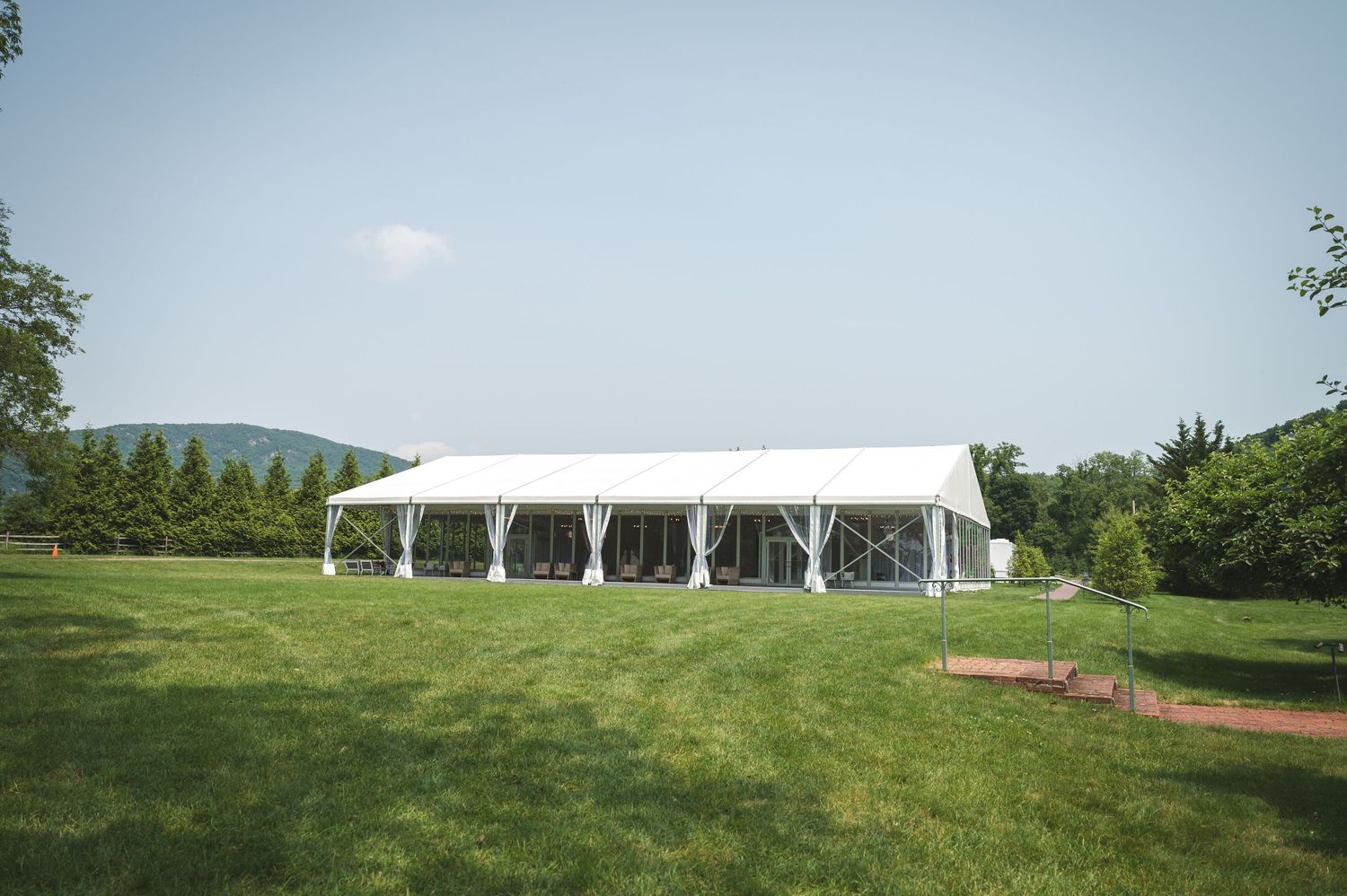 Modern white pavilion wedding tent set up on a green lawn with rolling hills and trees at Boscobel  House in Garrison, NY in Hudson Valley.