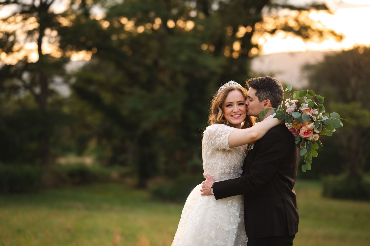 Hudson Valley wedding couple embrace during golden hour in a lush outdoor setting with a beautiful bouquet at The Garrison, Garrison NY.