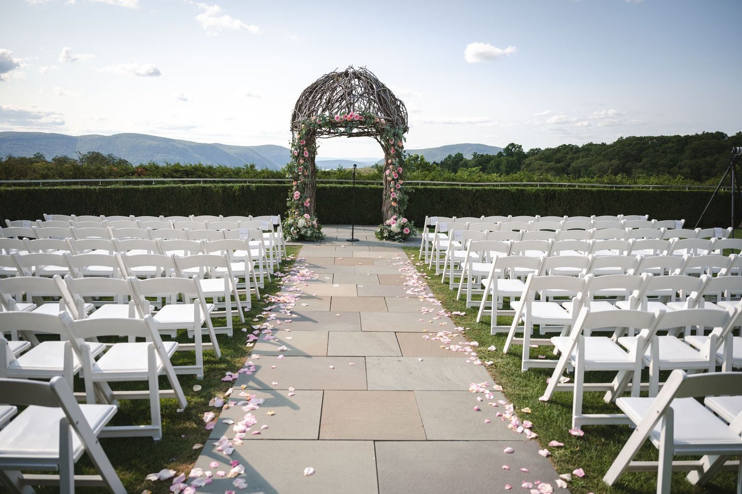 Wooden wedding arch with flowers and white chairs set up for outdoor ceremony with mountain views at The Garrison in Garrison, NY.