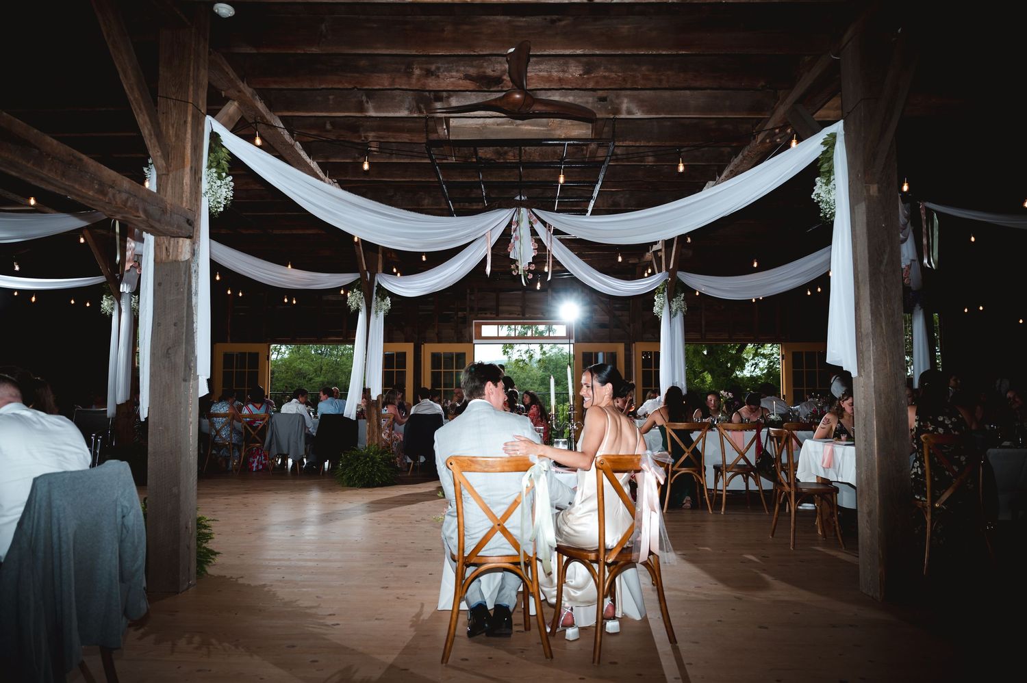 White drapes and string lights decorate a rustic wooden barn ceiling during reception at the Ruins at Sassafras in the Hudson Valley, NY.
