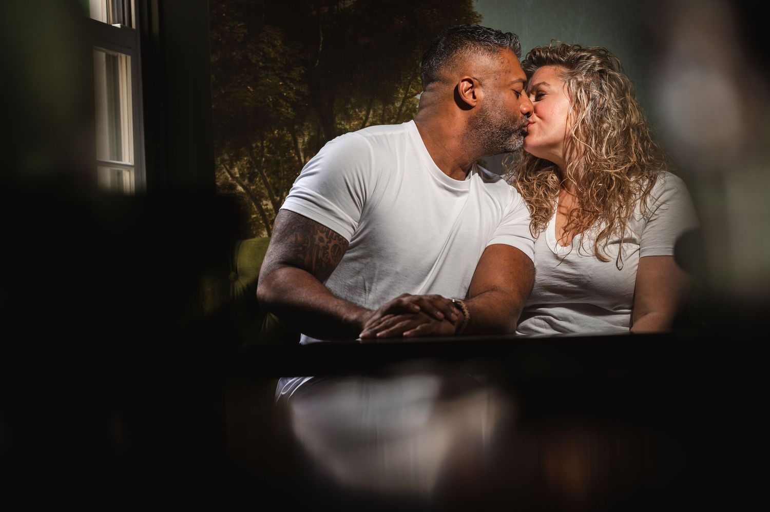 A romantic couple shares an intimate moment on a dark leather couch near a window.