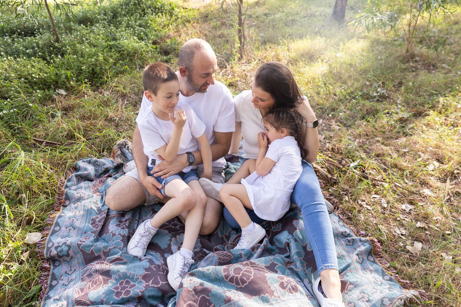 A family sits together on a patterned blanket during an outdoor photoshoot.