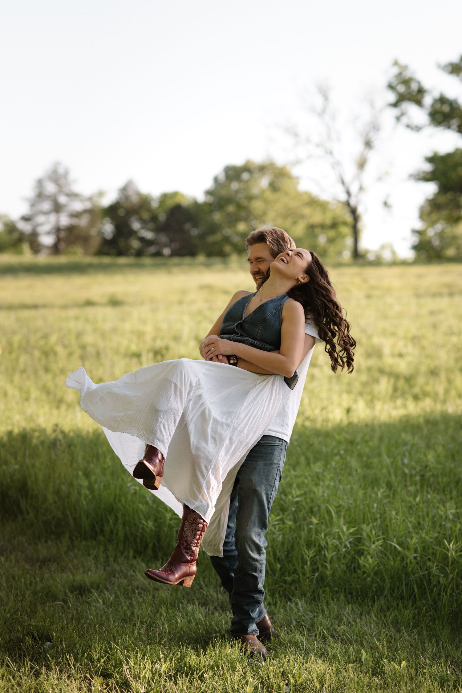 A romantic couple embraces in a sunlit meadow, with the person in white being dipped gracefully in a dance-like pose.