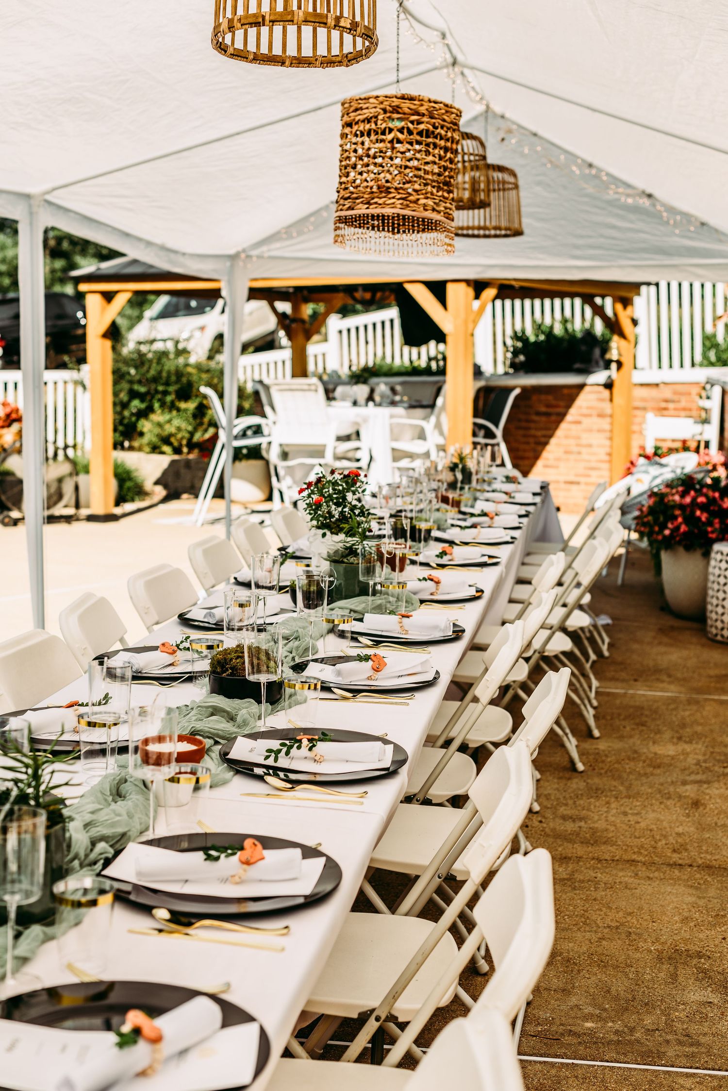 Elegant outdoor wedding reception setup with white folding chairs and rattan pendant lights under a white tent.