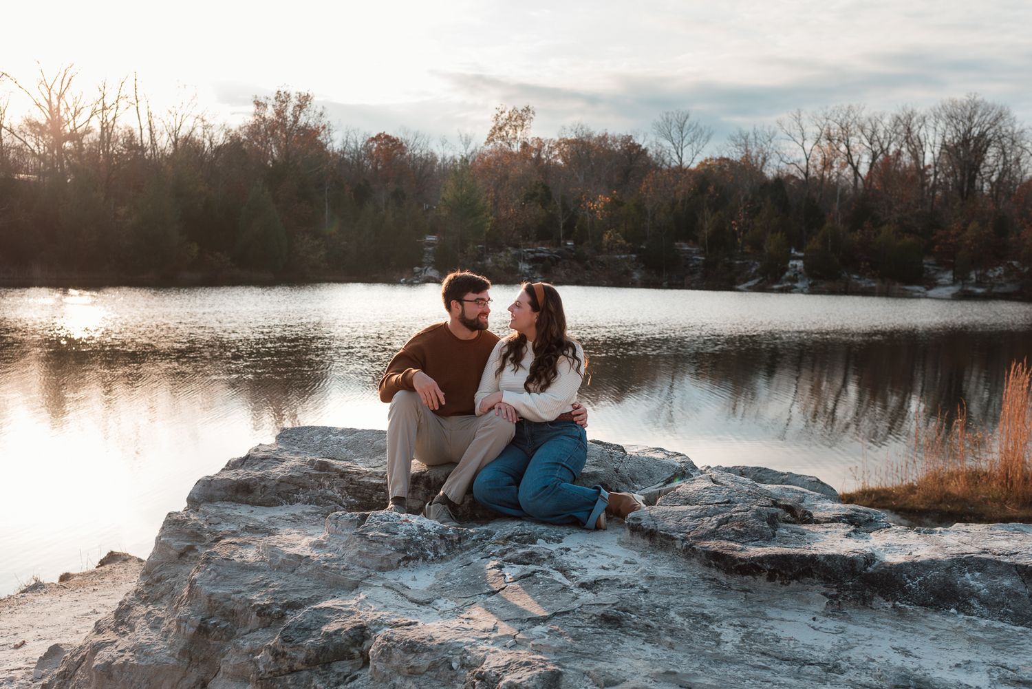 Couple shares intimate moment on rocky outcrop by serene lake at sunset.