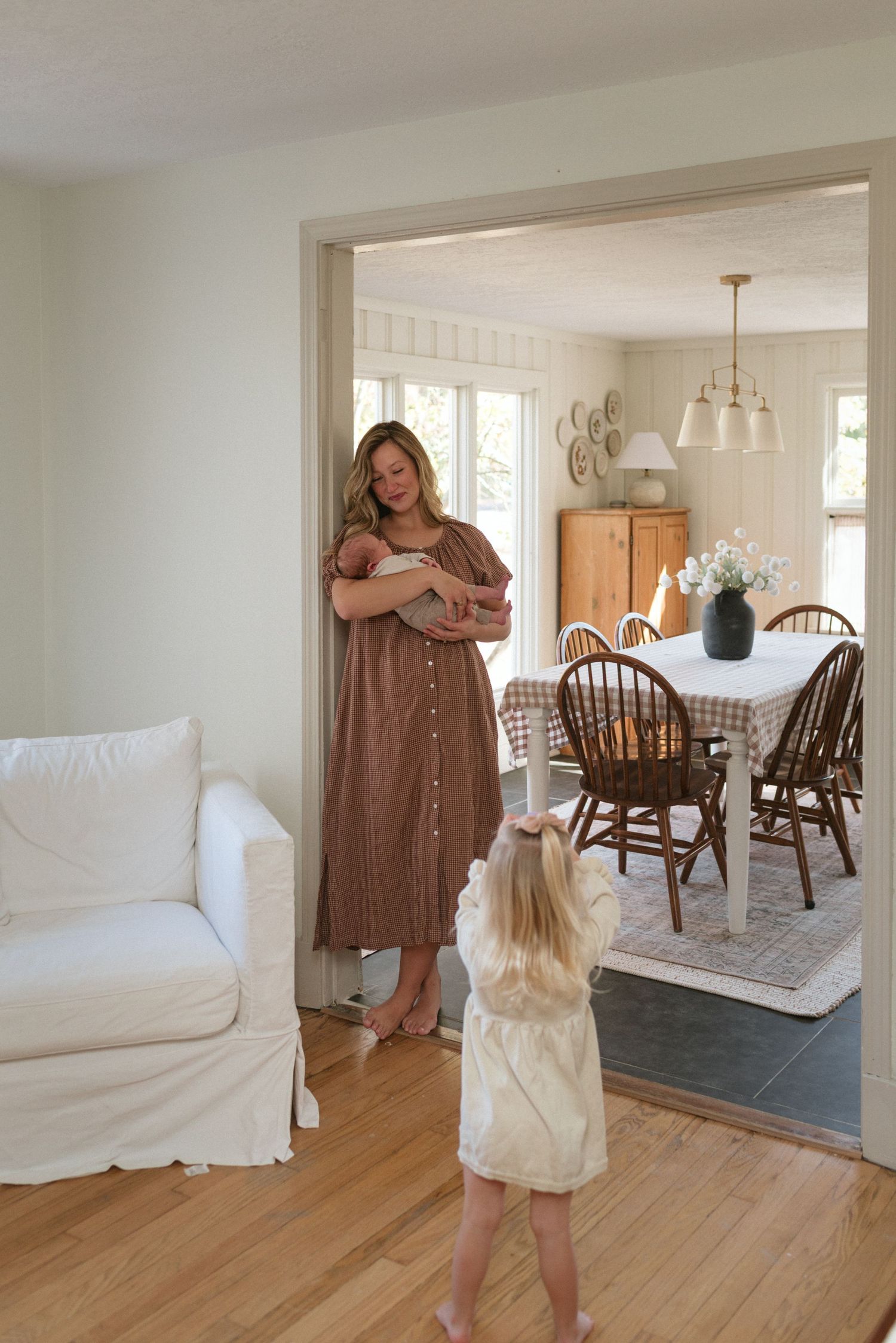 A cozy living and dining room interior with hardwood floors, white furniture, and a rustic wooden dining set.