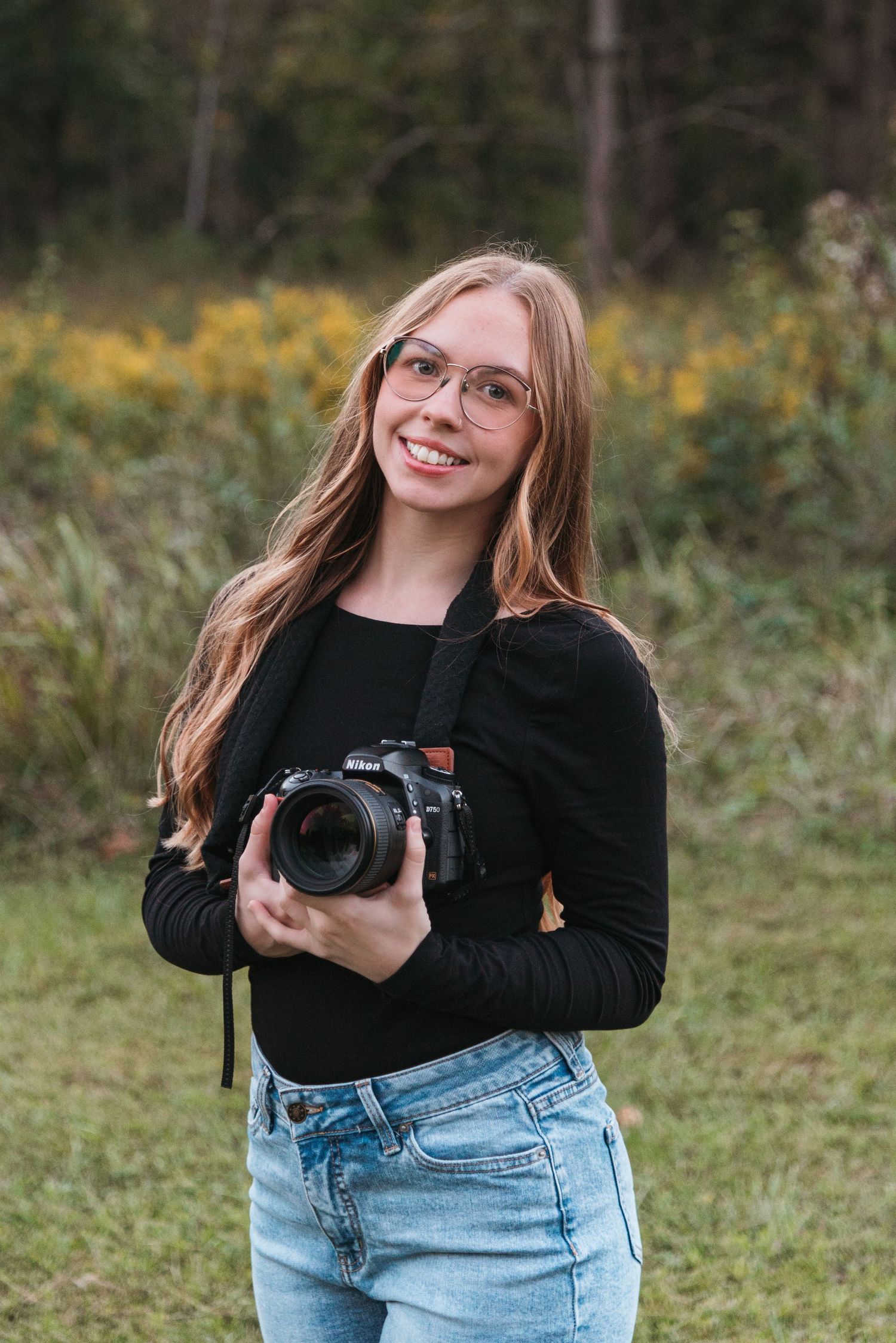 Photographer in casual attire holding a professional camera in an outdoor natural setting.