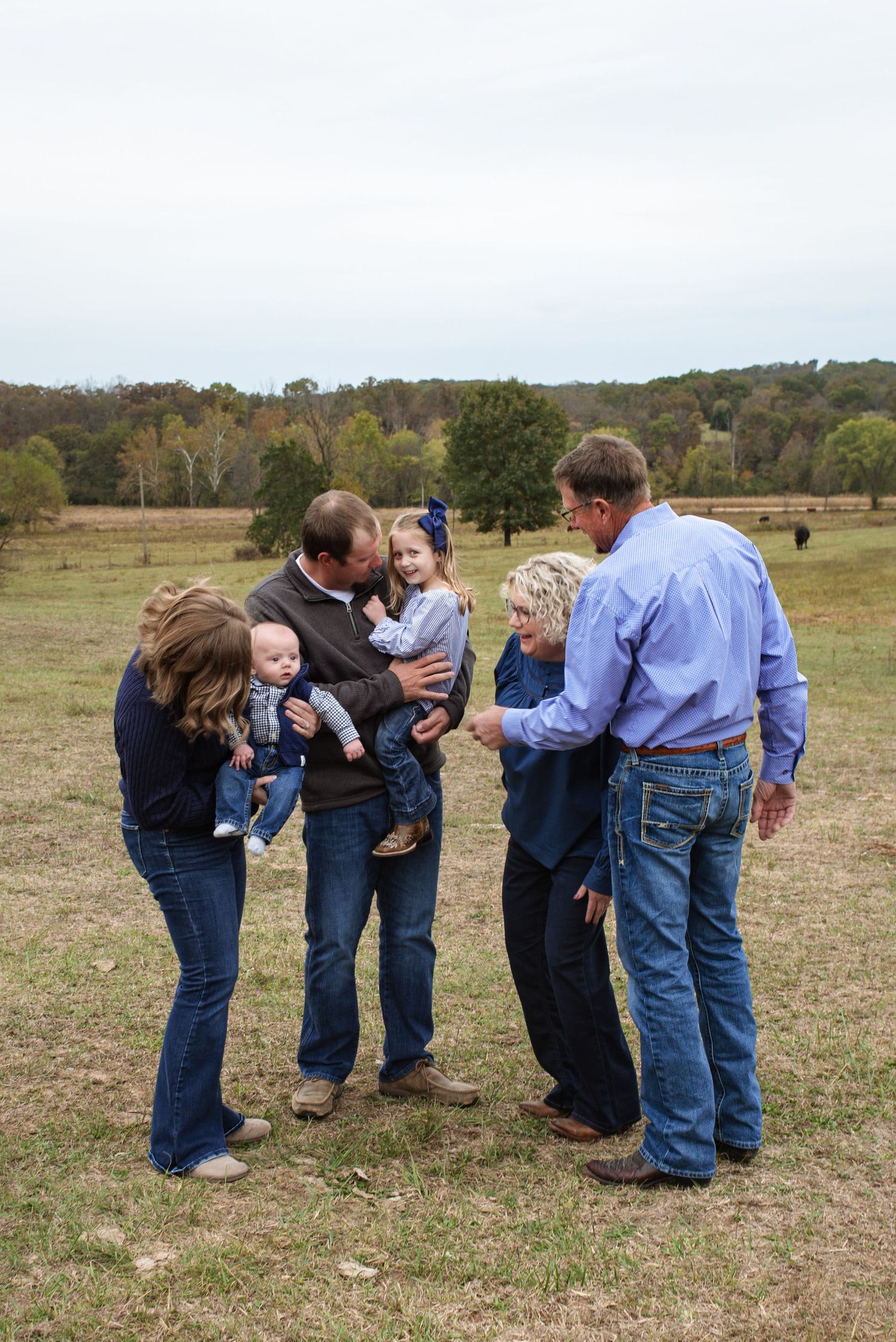 A family group stands together in a grassy field on an autumn day with rolling hills in the background.