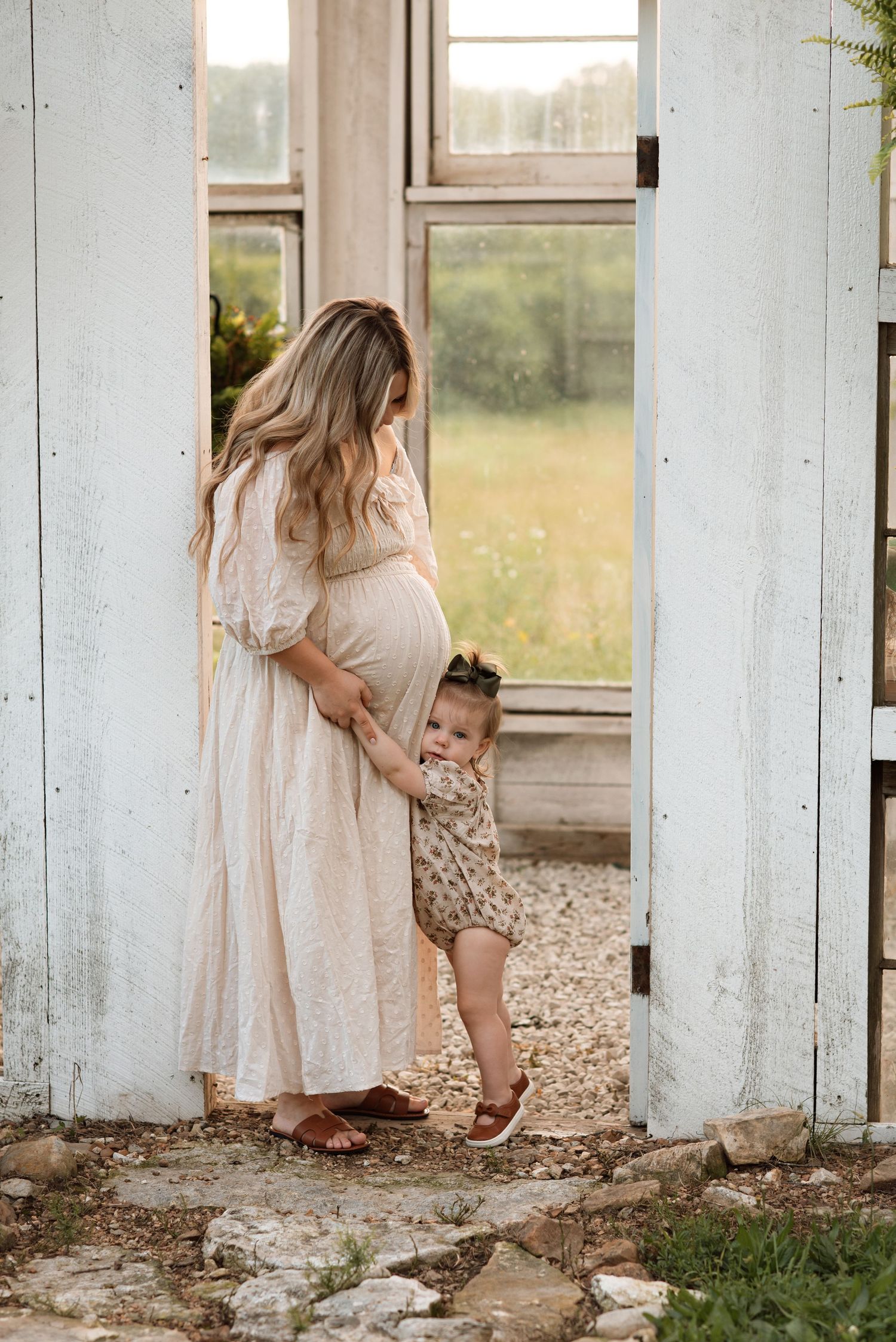 A tender moment between an expecting mother in a flowing dress and small child standing in a rustic doorway.