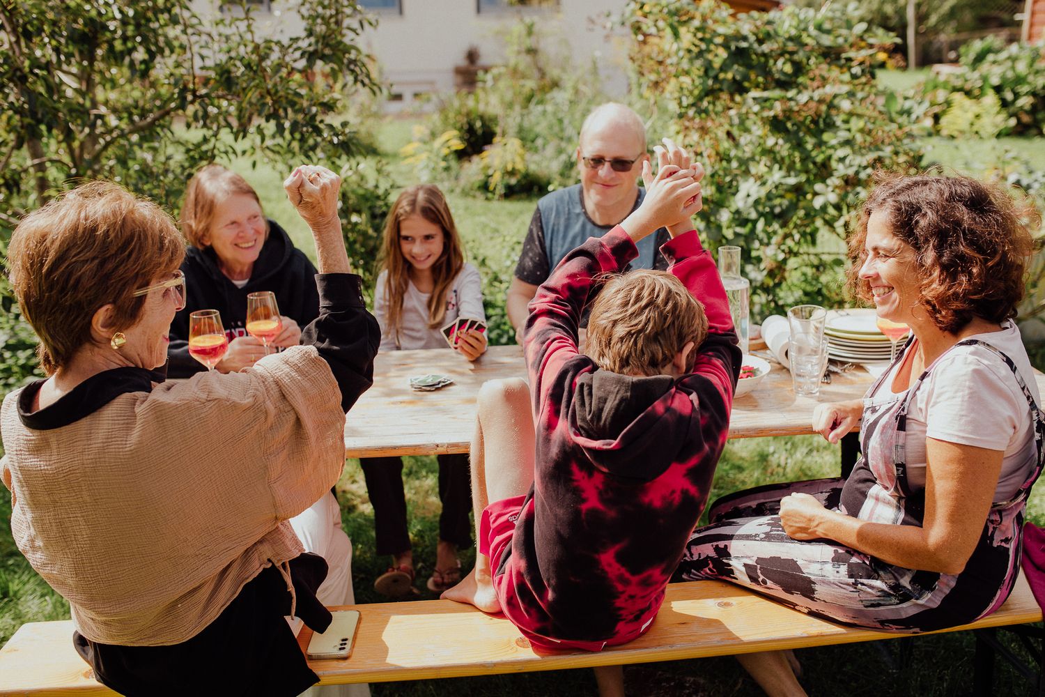 Eine Gruppe versammelt sich an einem Picknicktisch in einem sonnigen Gartensetting und genießt gemeinsam Essen und Gespräche.