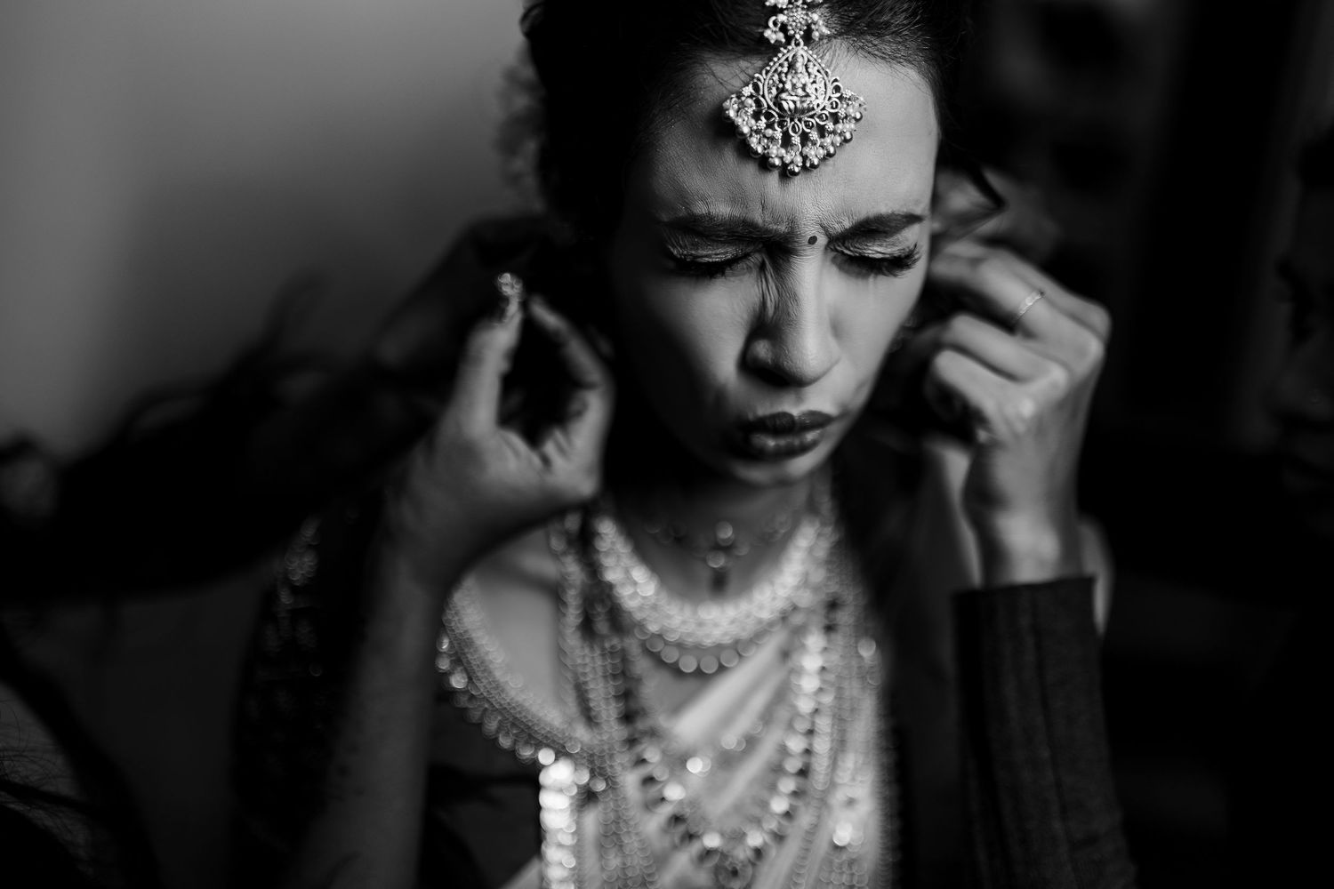Black and white portrait of a bride wearing traditional Indian jewelry and pearl necklaces in a candid moment.