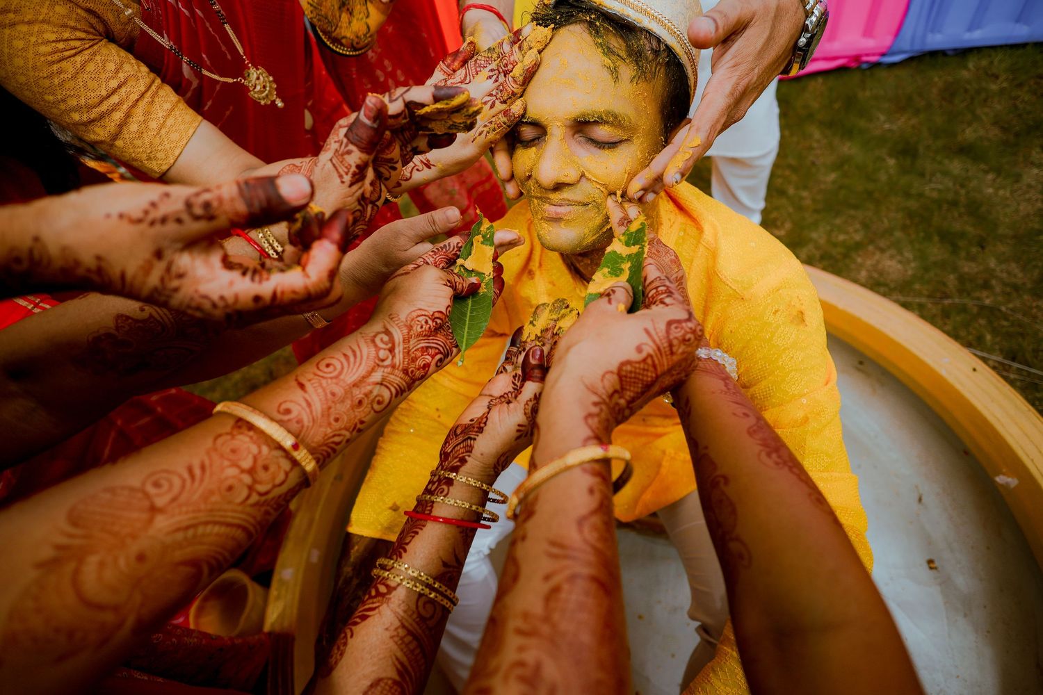 Hands adorned with intricate henna designs help dress someone in traditional yellow Indian wedding attire.