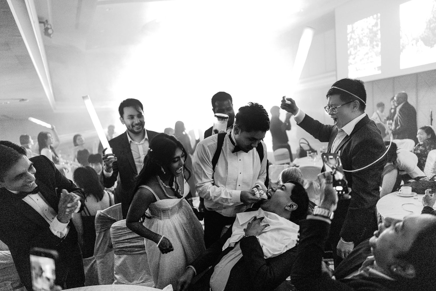 Black and white wedding reception photo showing guests celebrating with glow sticks on the dance floor.