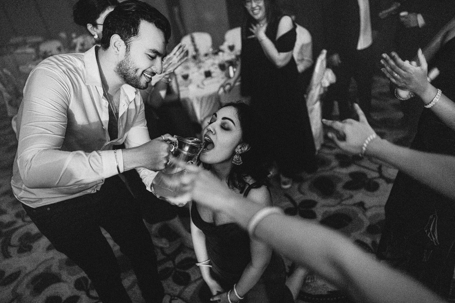 Black and white photo of guests celebrating at a wedding reception, sharing drinks on the dance floor.