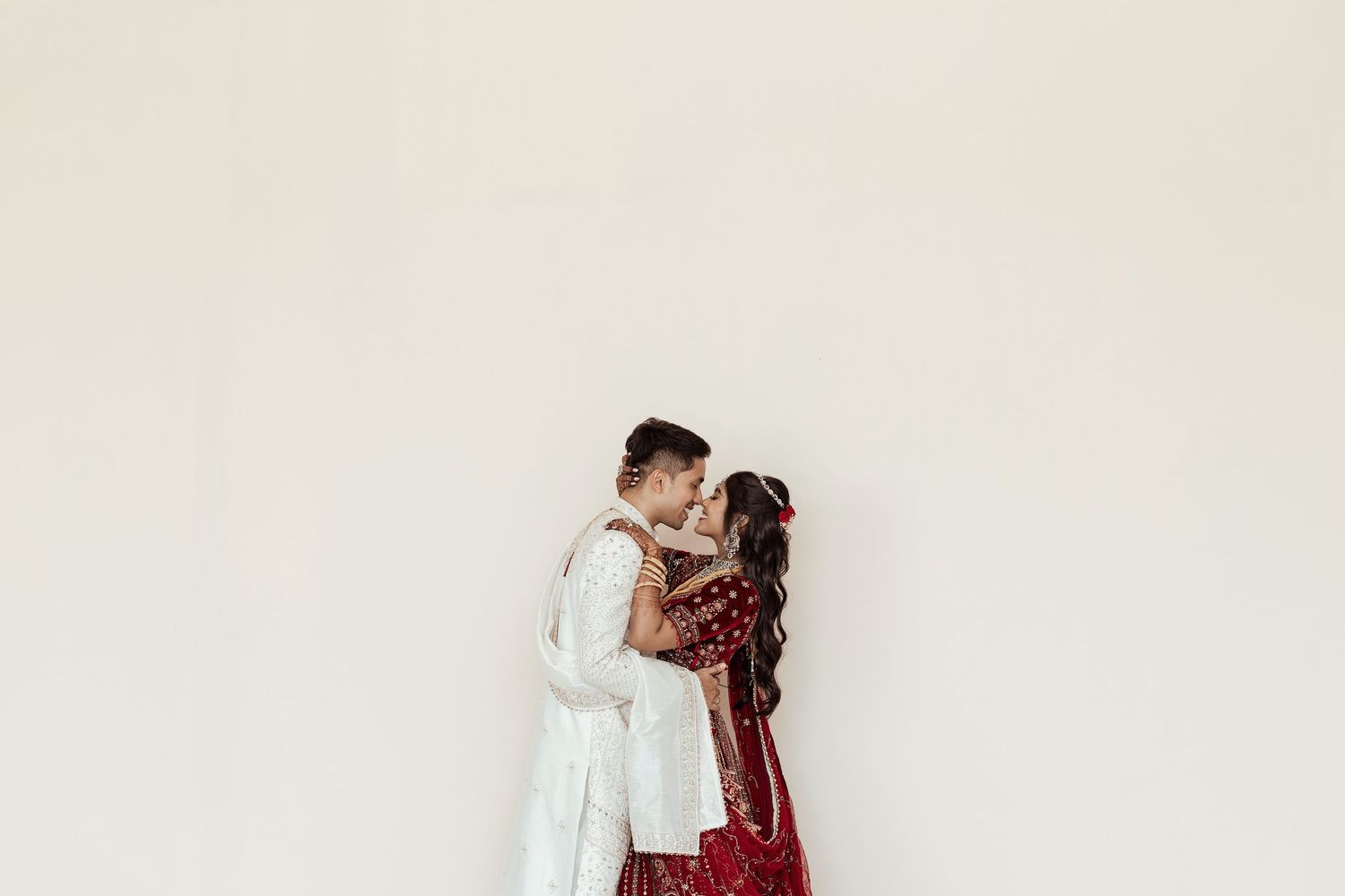Couple in traditional Indian wedding attire sharing a romantic kiss against a white background.