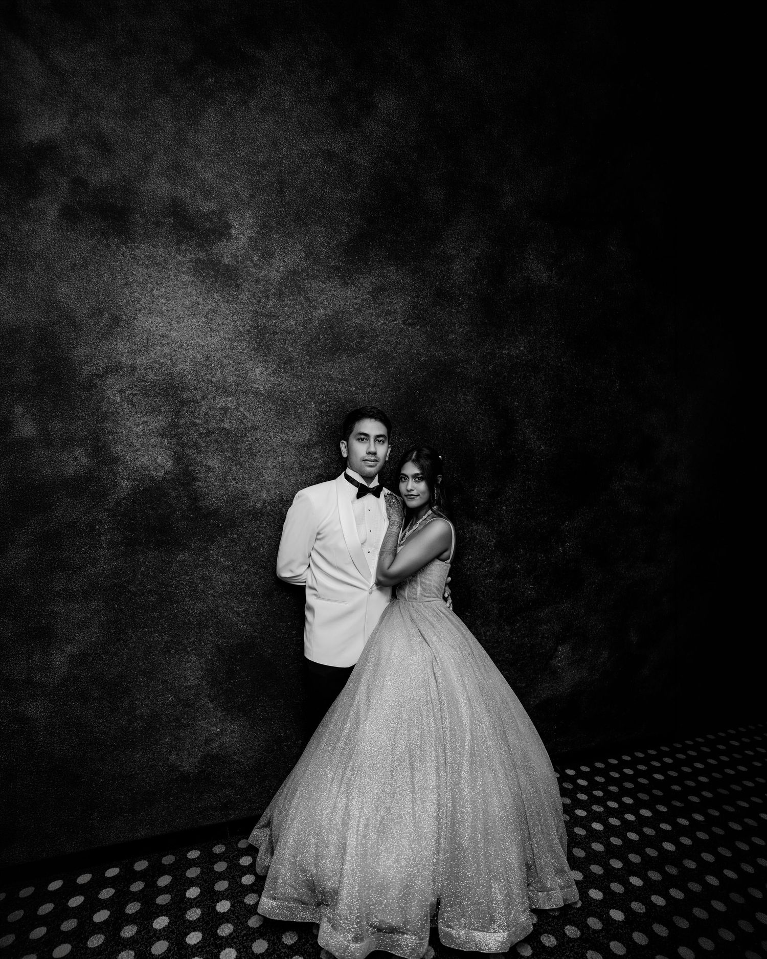 Black and white photo of a couple posing elegantly, man in white tuxedo and woman in a ball gown.