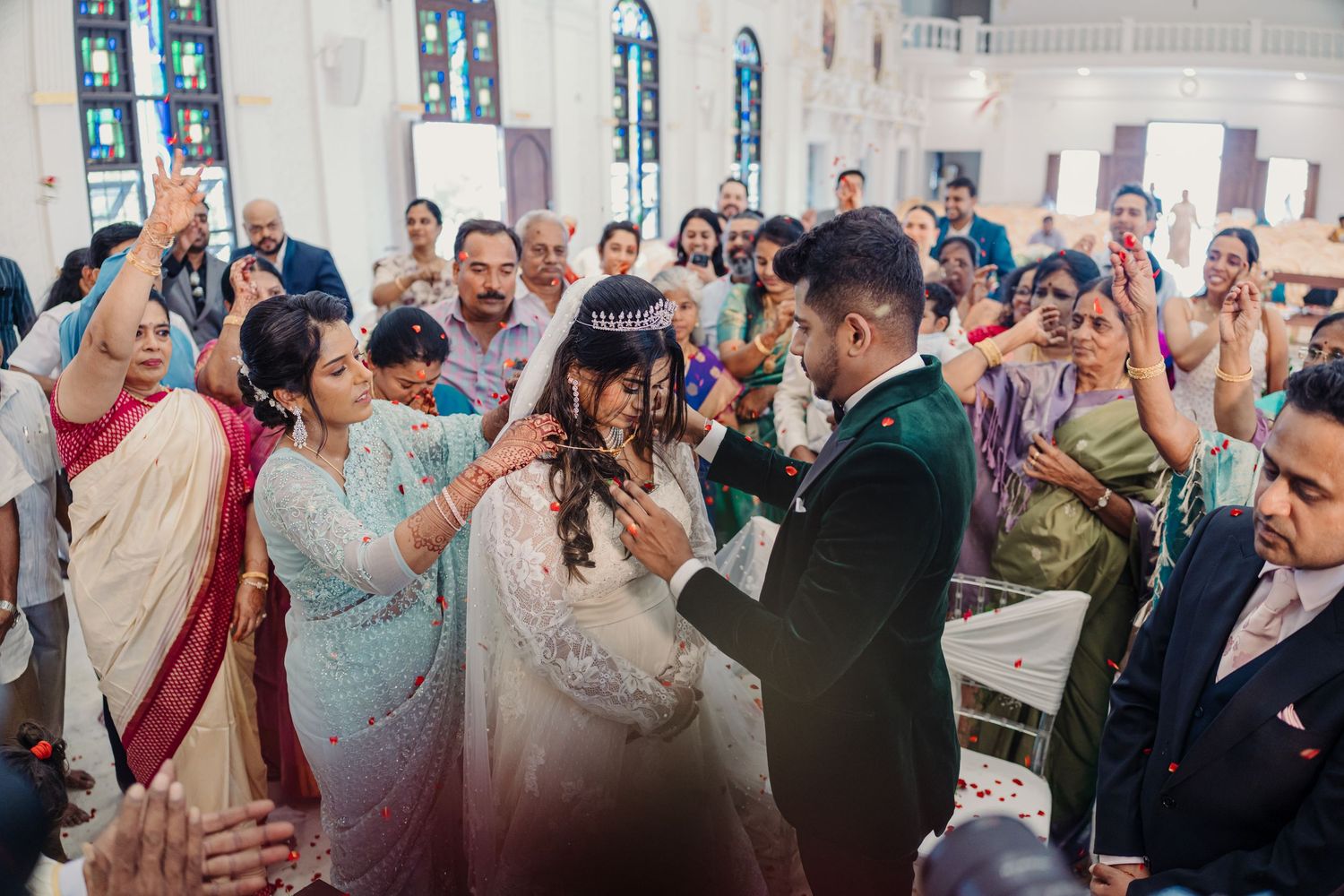 Large group celebrating at a wedding reception in a church hall with stained glass windows.