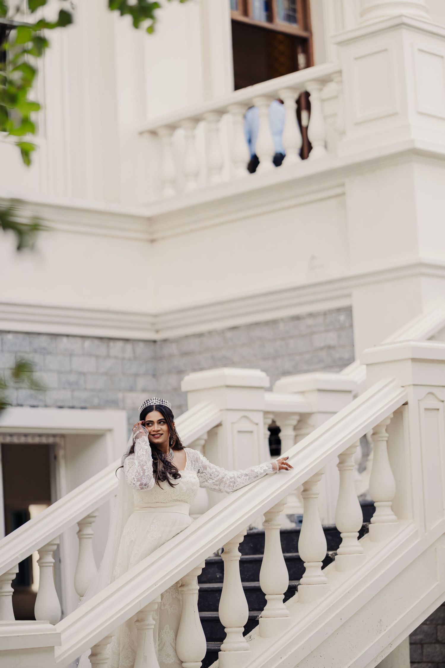 Bride in white dress poses on elegant white marble staircase of a classic building.