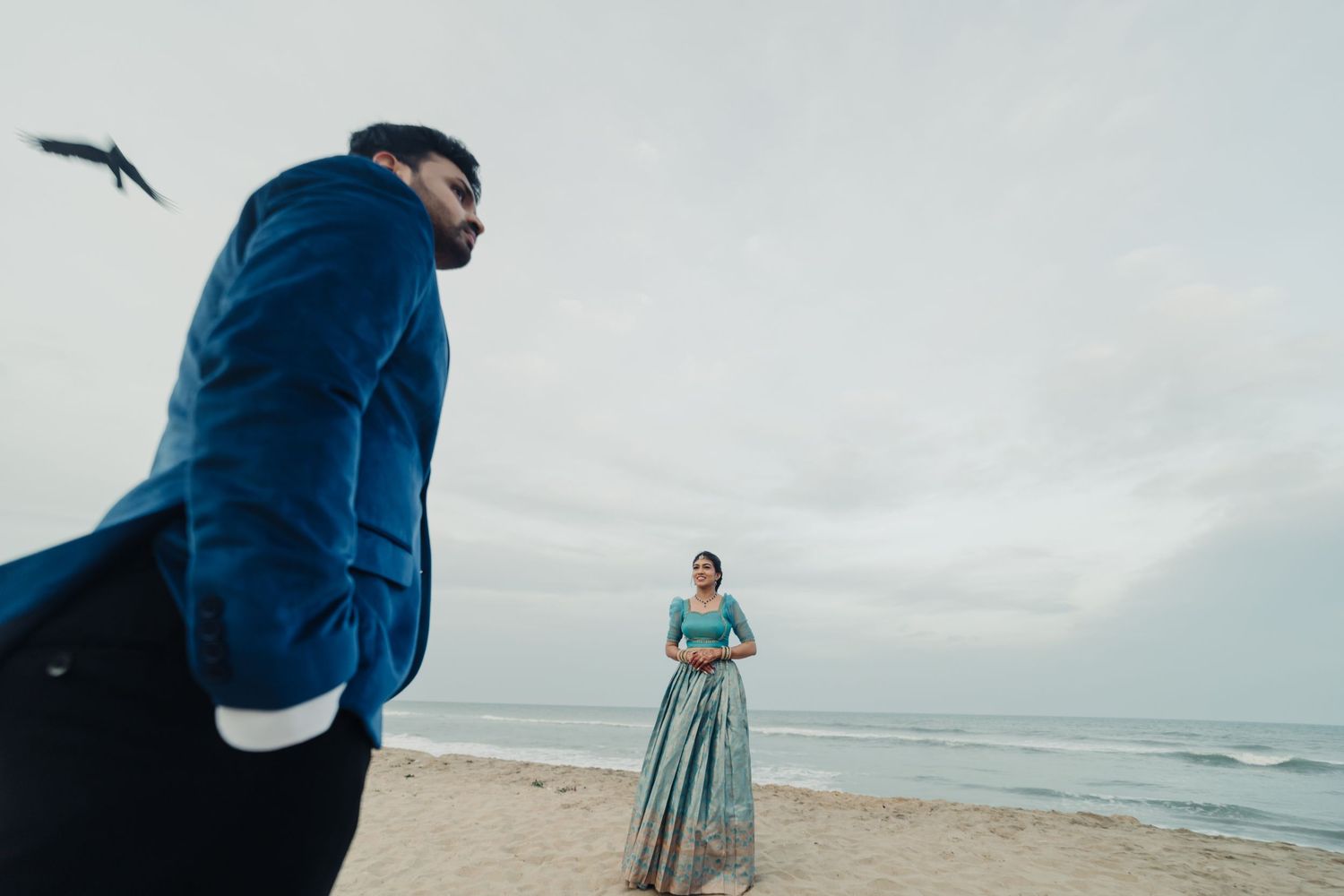 A couple stands on a beach during an overcast day, creating a romantic coastal atmosphere.
