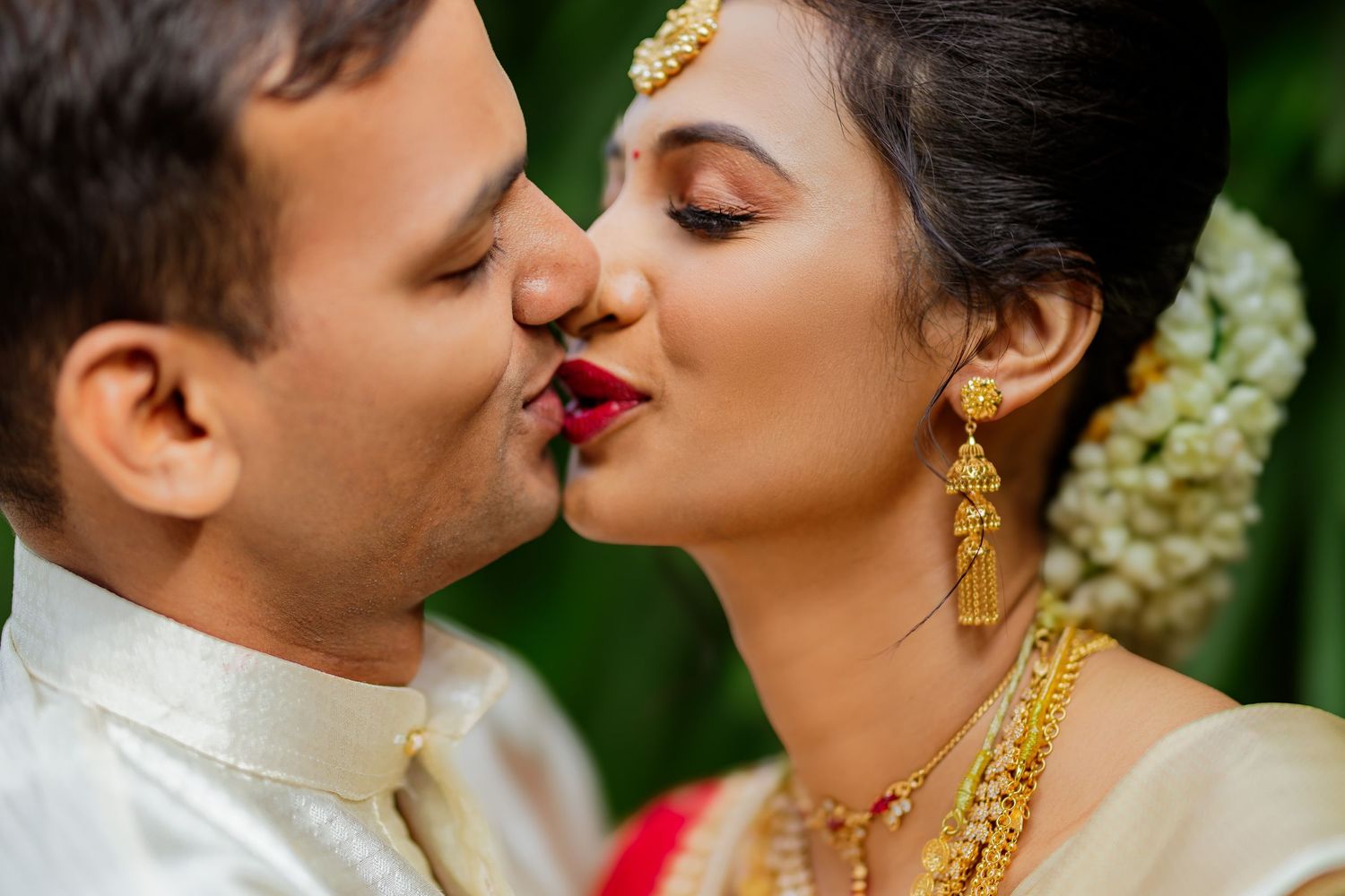 A romantic wedding couple shares a tender kiss while wearing traditional South Asian wedding attire and jewelry.