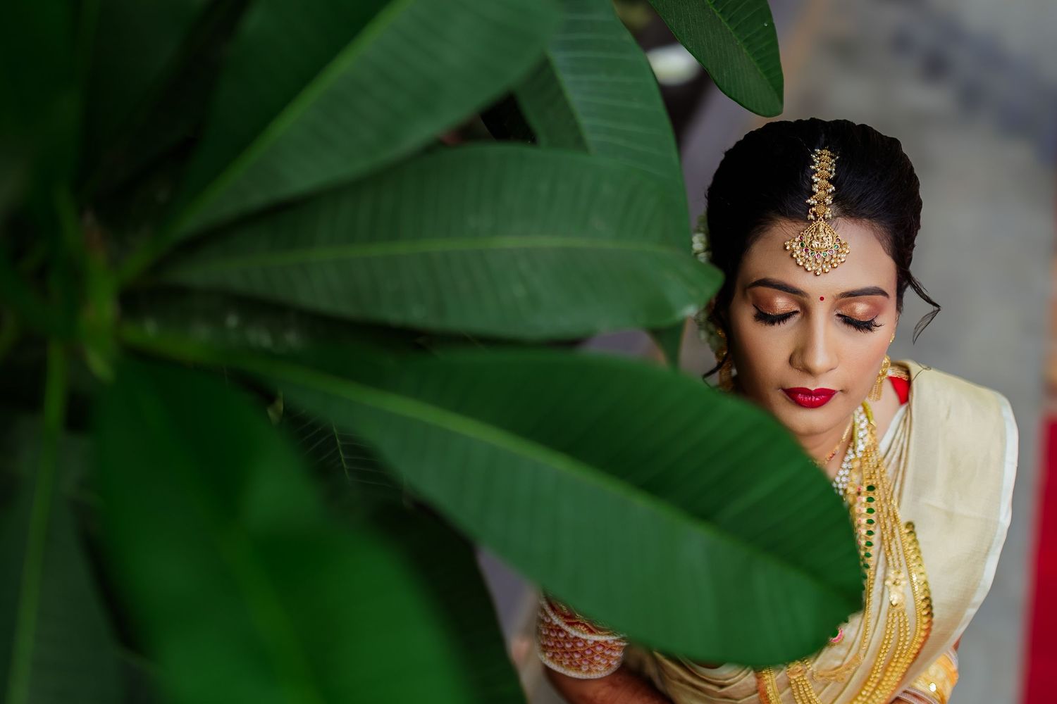 A traditional Indian bride adorned in gold jewelry and yellow saree sits during a wedding ceremony preparation.