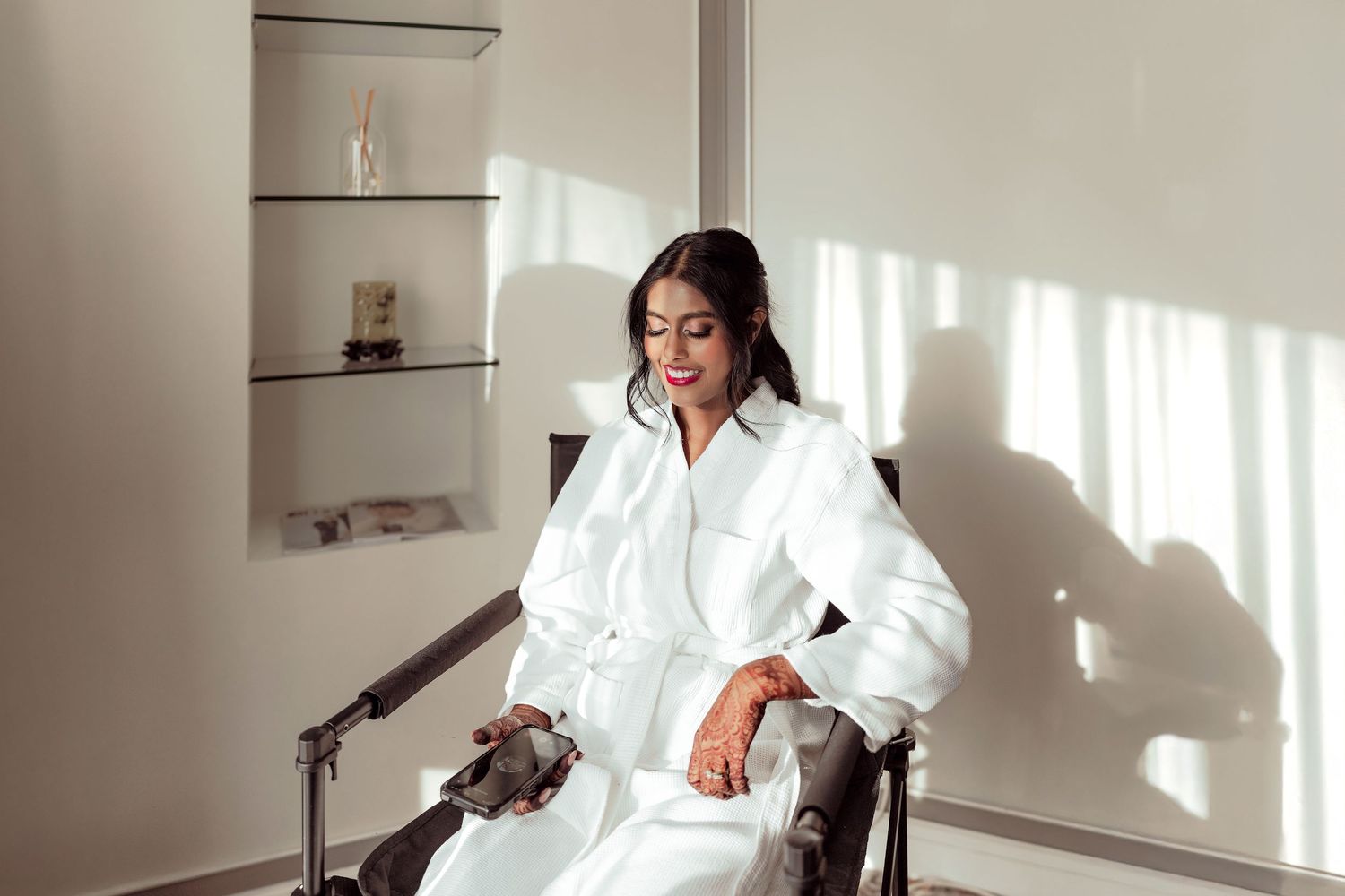 Woman in white robe sitting relaxed in a modern chair, bathed in natural sunlight in a minimalist room.