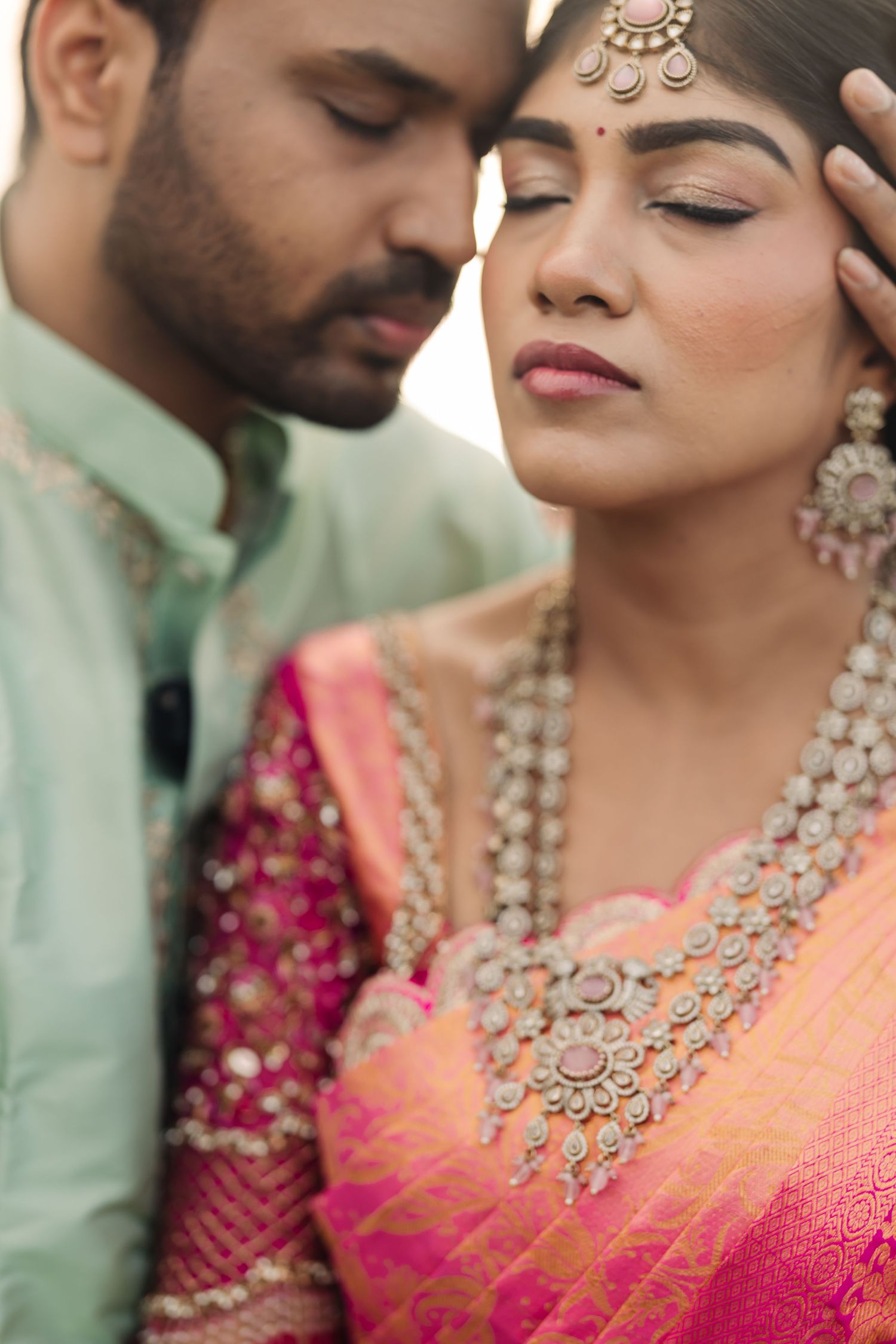 Close-up of traditional Indian wedding jewelry and attire in vibrant pink and mint colors.