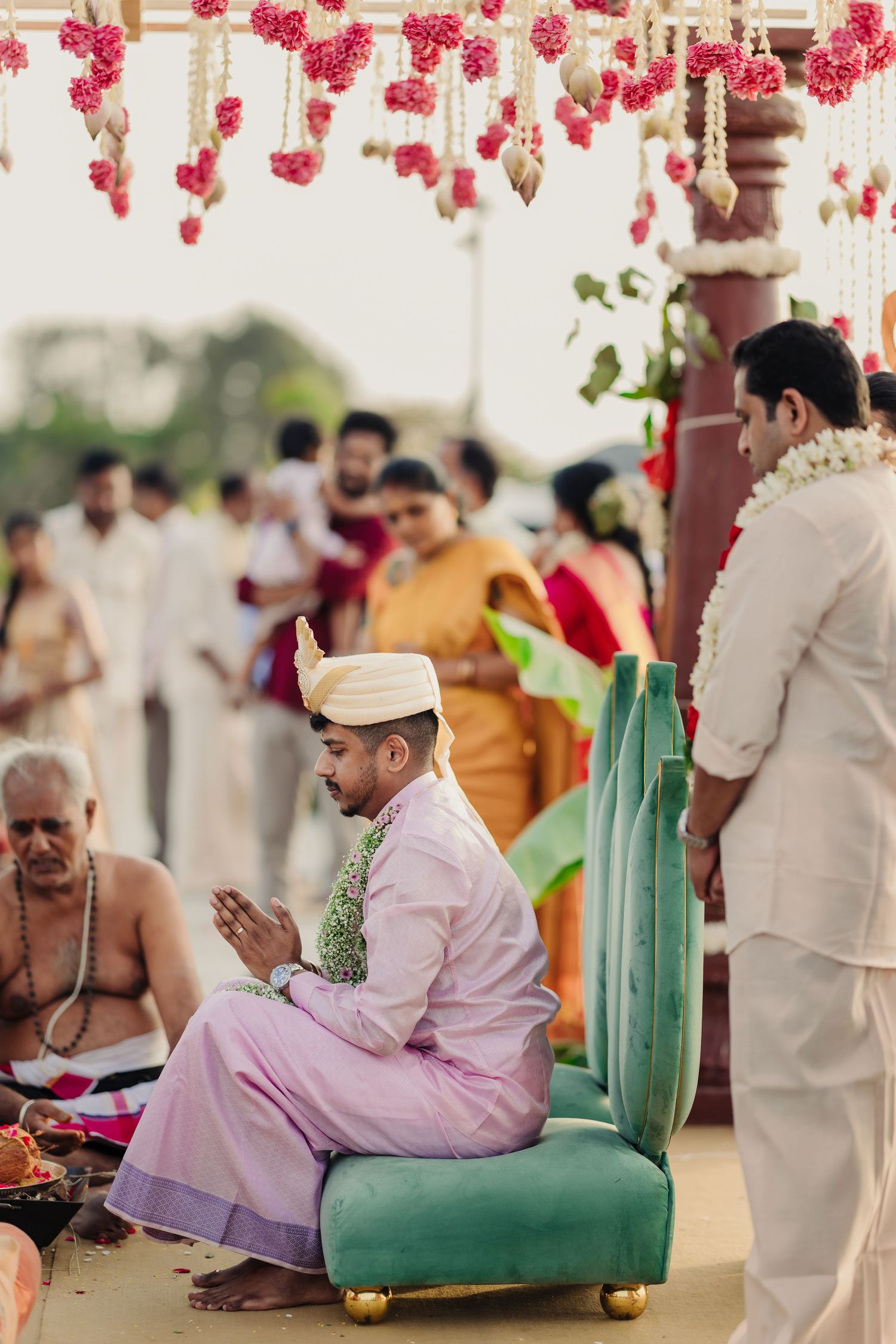 Traditional Indian wedding ceremony setup with pink floral decorations and guests seated on green chairs.